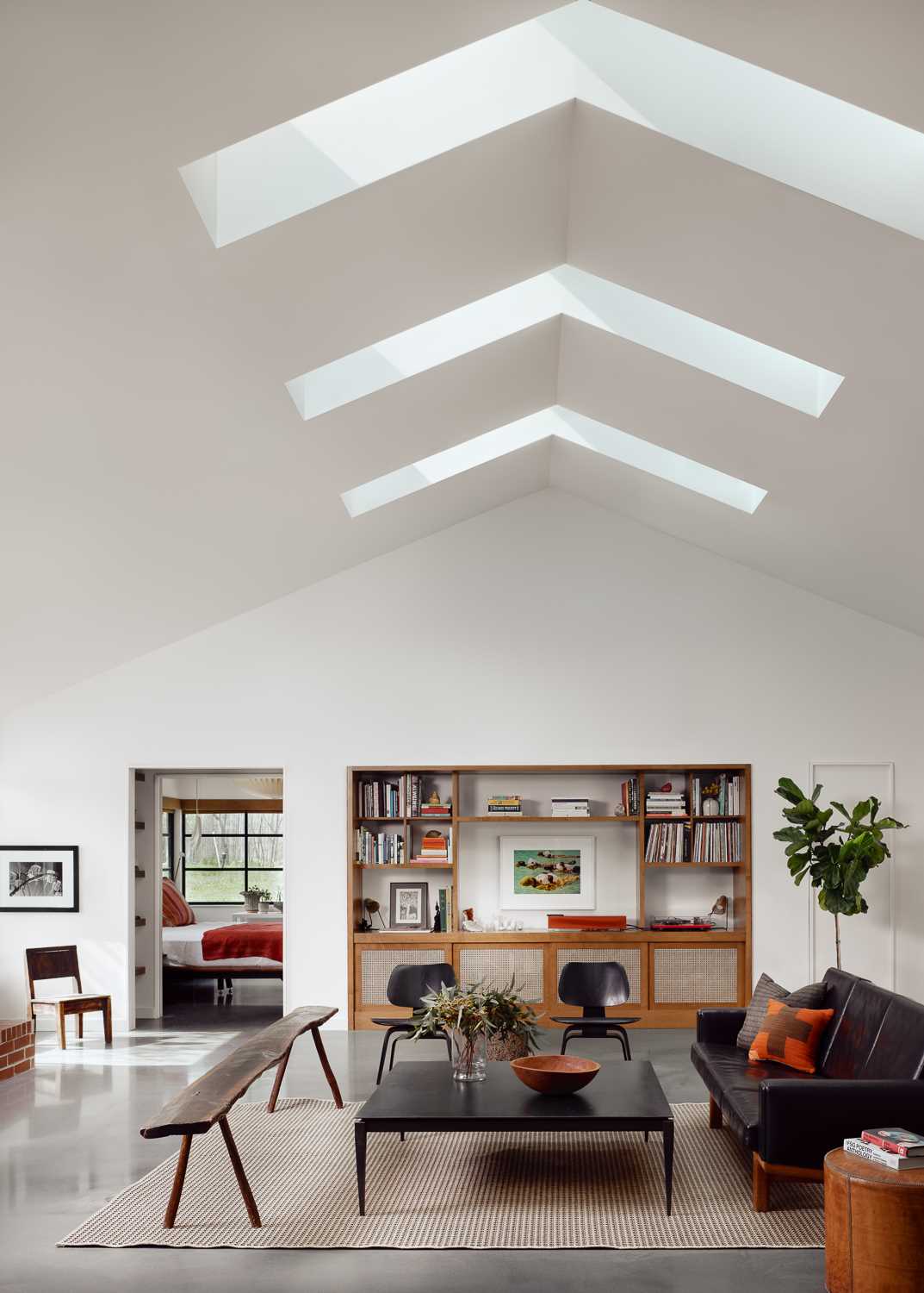 Inside this renovated home, the living room is an open and lofty space filled with natural light from multiple skylights straddling the vaulted ridge, while built-in wood cabinets and shelving add warmth to the interior.