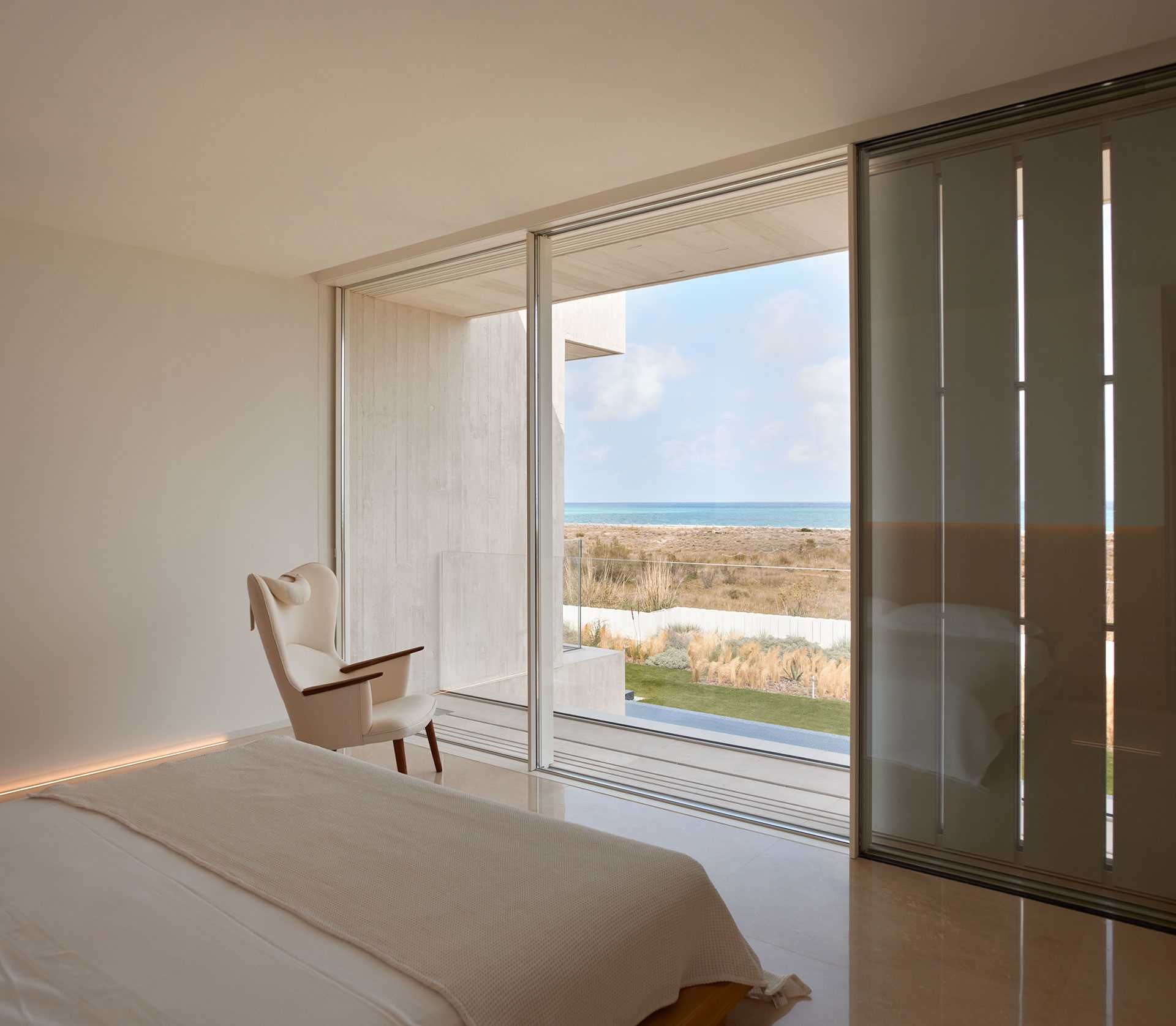 A modern bedroom with a neutral color palette and views of the water.