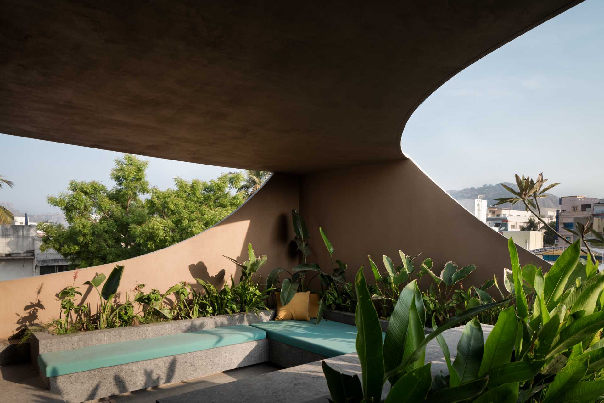 Upstairs in this modern home, there's a bedroom and a living room that both enjoy the views due to the cut-outs, while the balconies have built-in seating and planters that add greenery to the concrete surrounds.