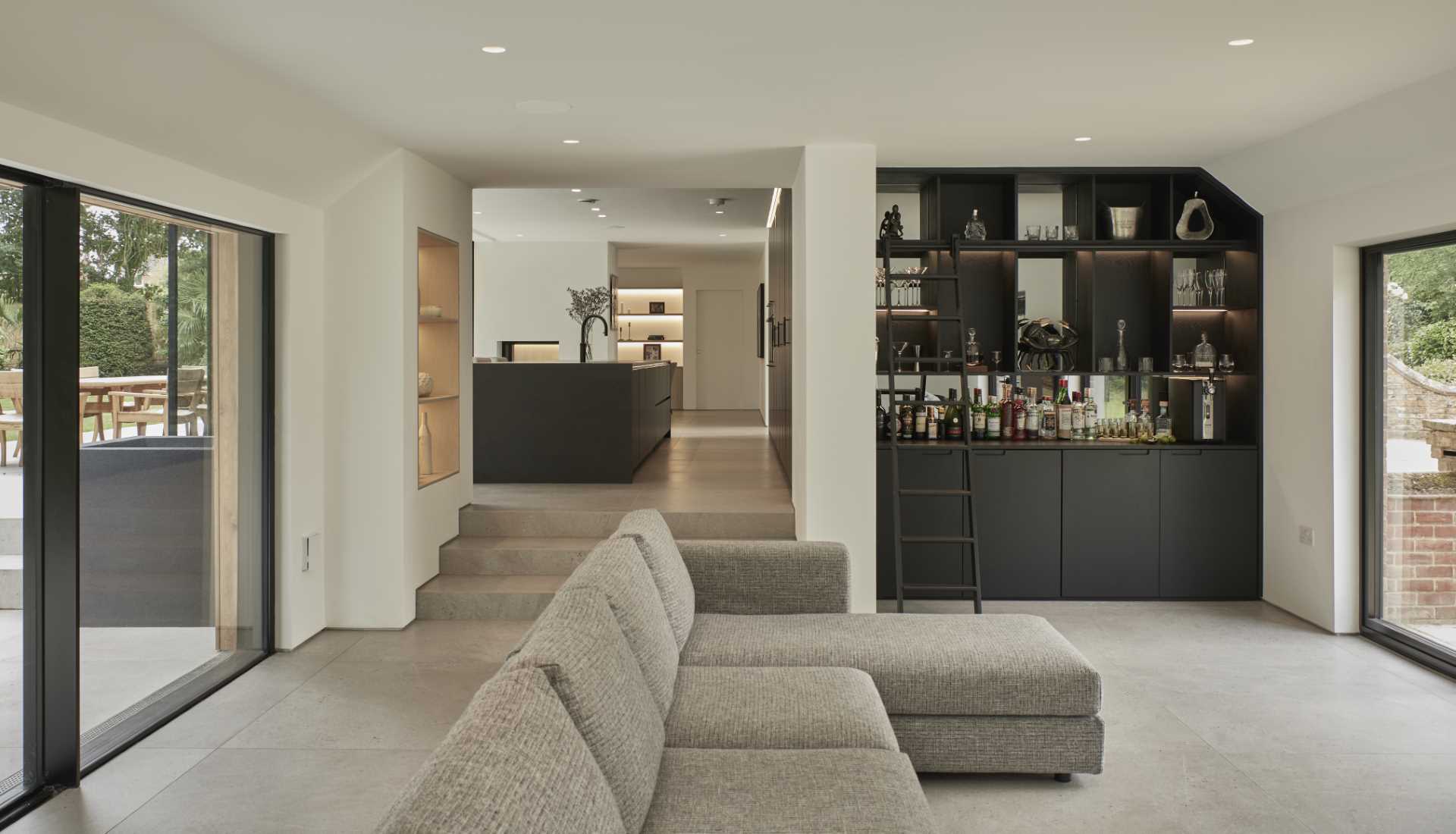 This modern living room includes a built-in bar, while steps with built-in shelving on the adjacent wall, lead up to the kitchen.