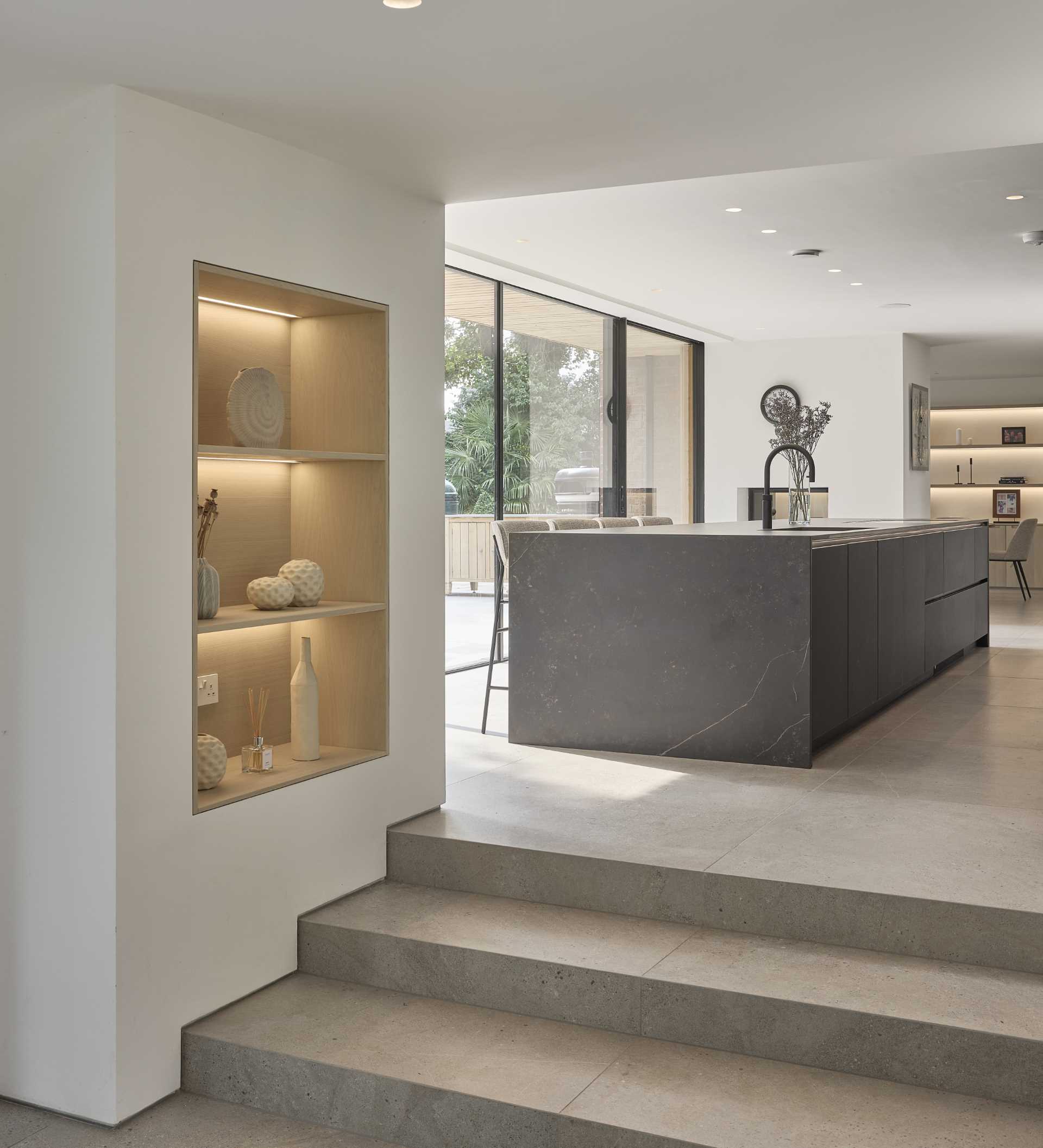 This modern living room includes a built-in bar, while steps with built-in shelving on the adjacent wall, lead up to the kitchen.