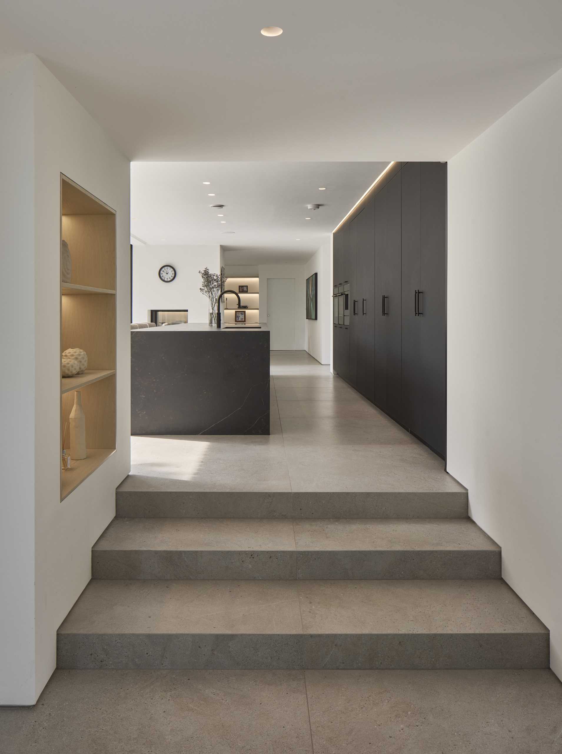 This modern living room includes a built-in bar, while steps with built-in shelving on the adjacent wall, lead up to the kitchen.