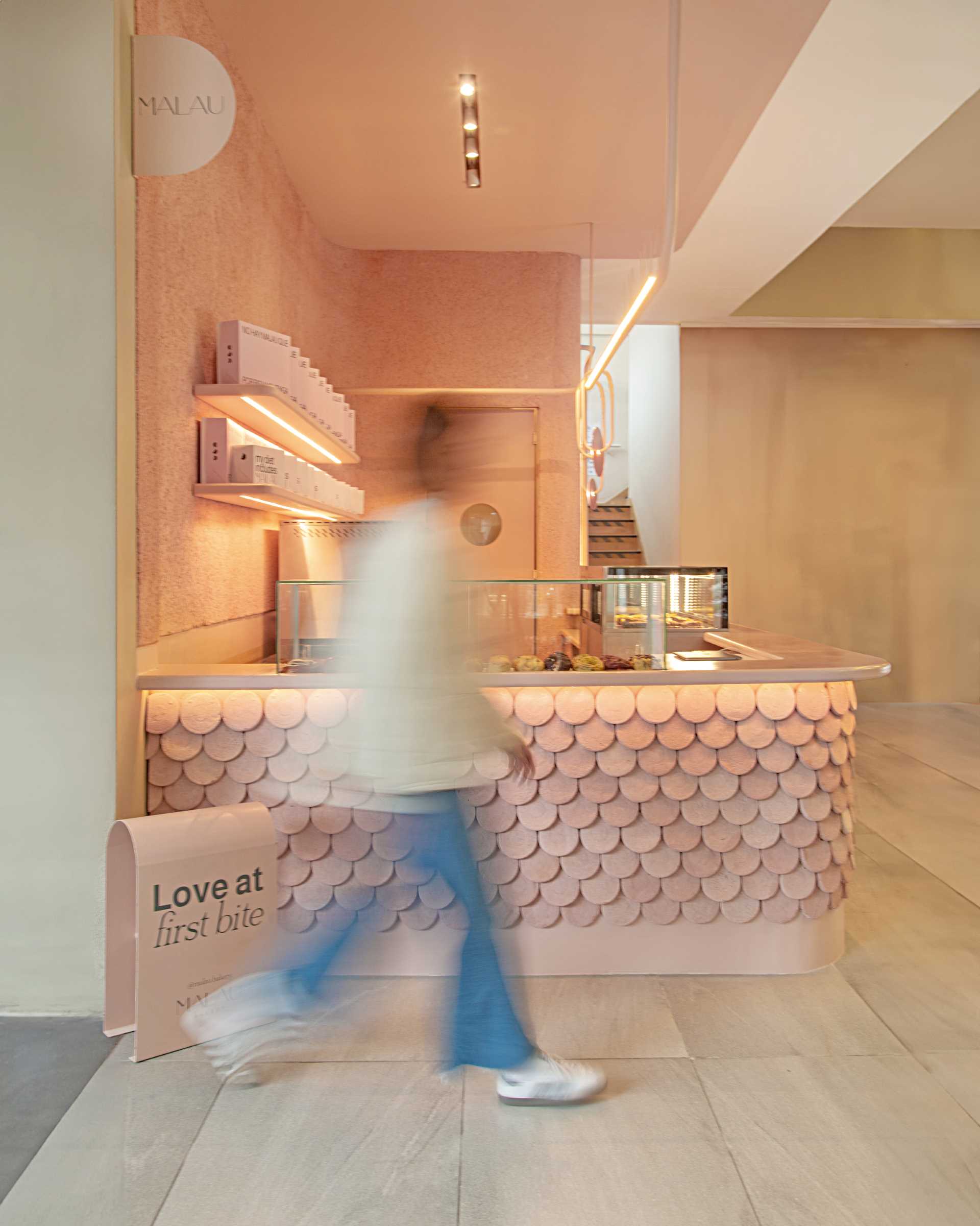 A modern bakery with a pastel pink colour palette, also includes handcrafted pieces of dyed cement that make up the cladding of the bar front.