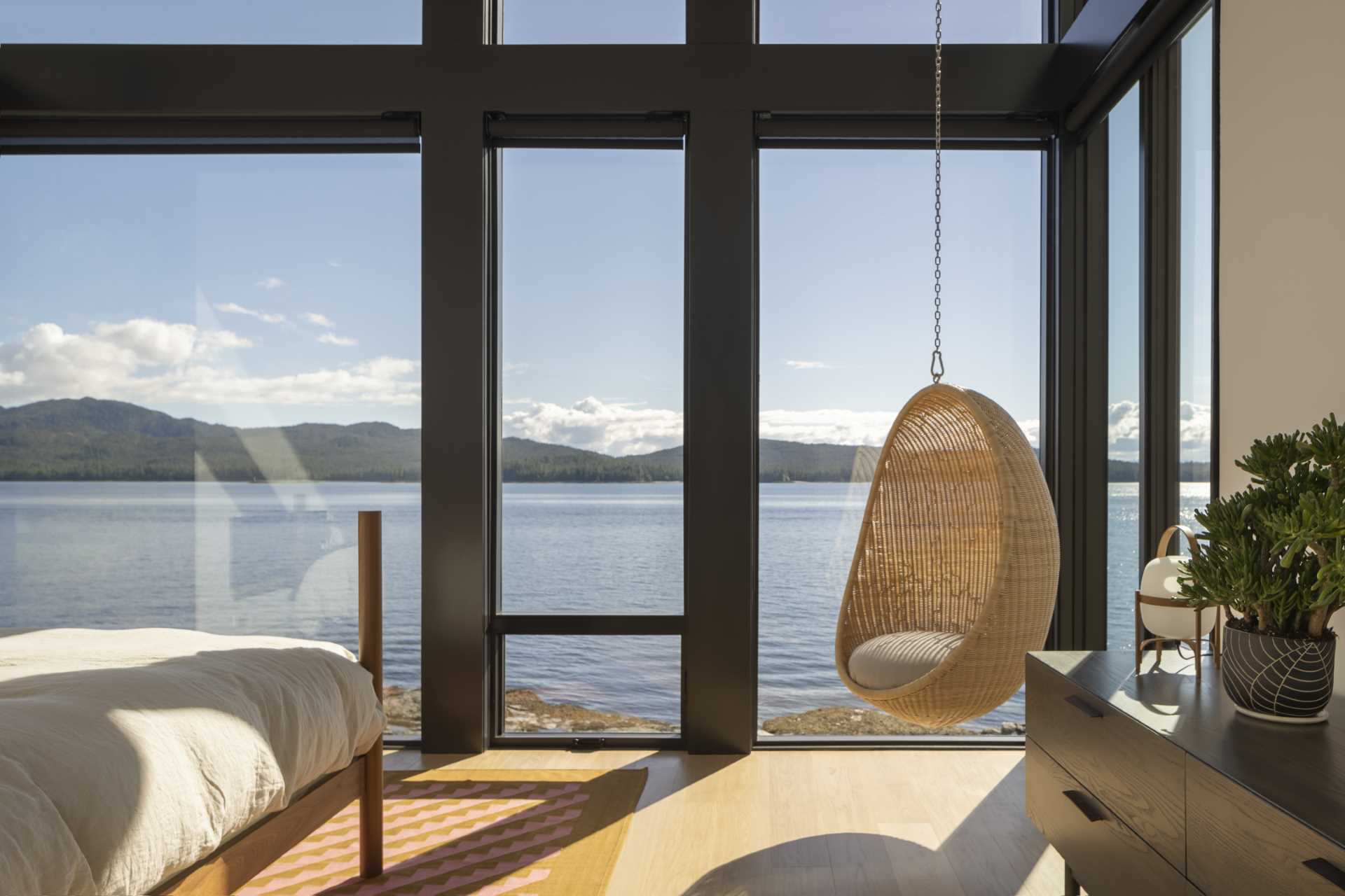 In this bedroom, the walls of windows flood the room with natural light, while a hanging chair creates a cozy spot to enjoy the view.