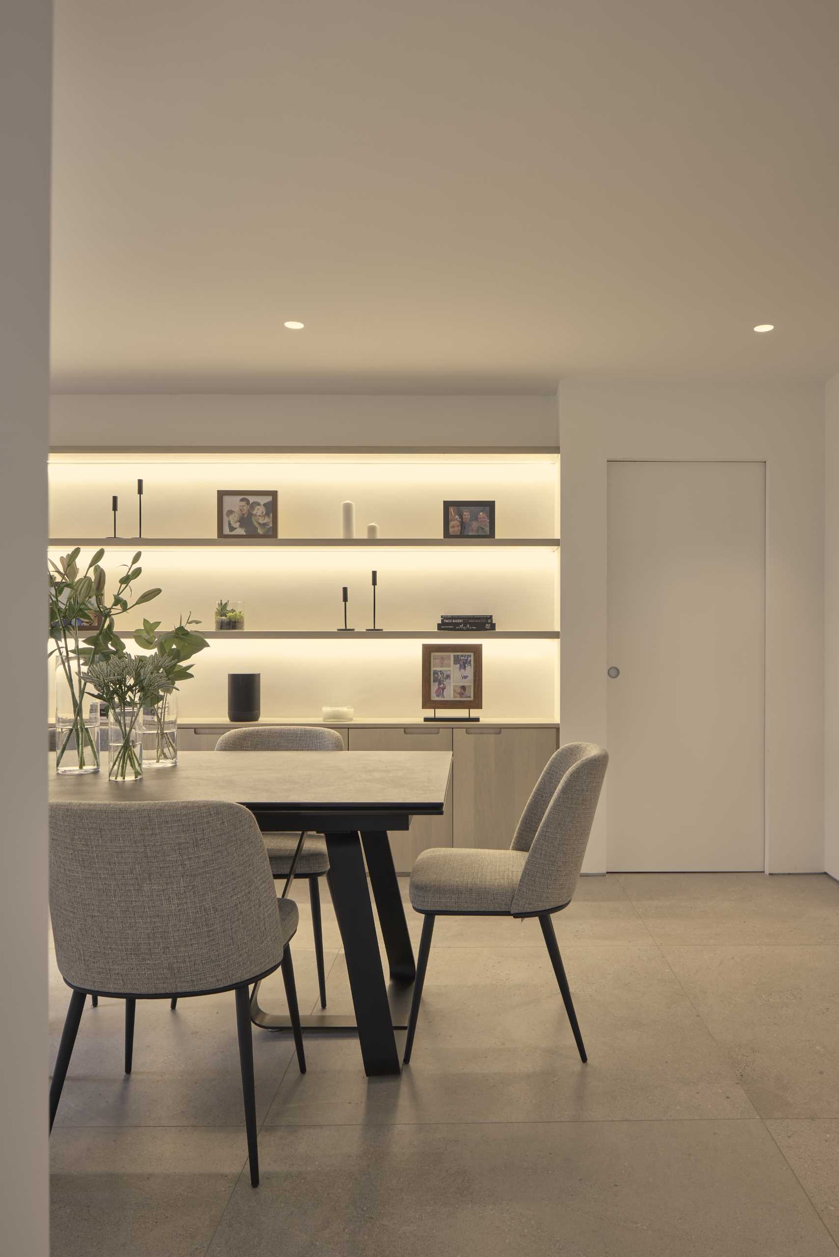 In this modern dining room, hidden lighting showcases the shelving, white cabinetry provides additional storage.