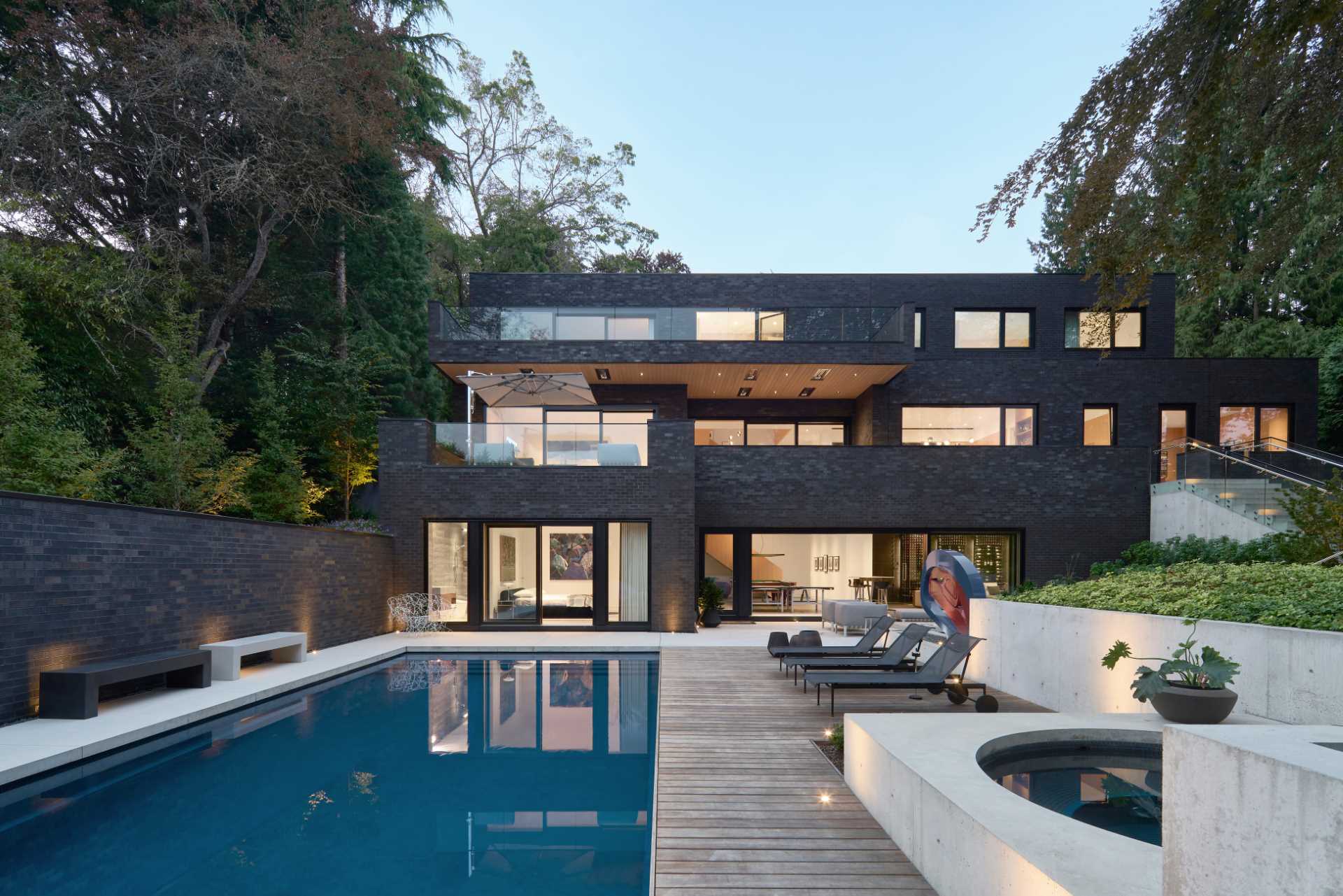 A modern house with a dark brick exterior includes an outdoor living room, BBQ area, deck, and swimming pool.