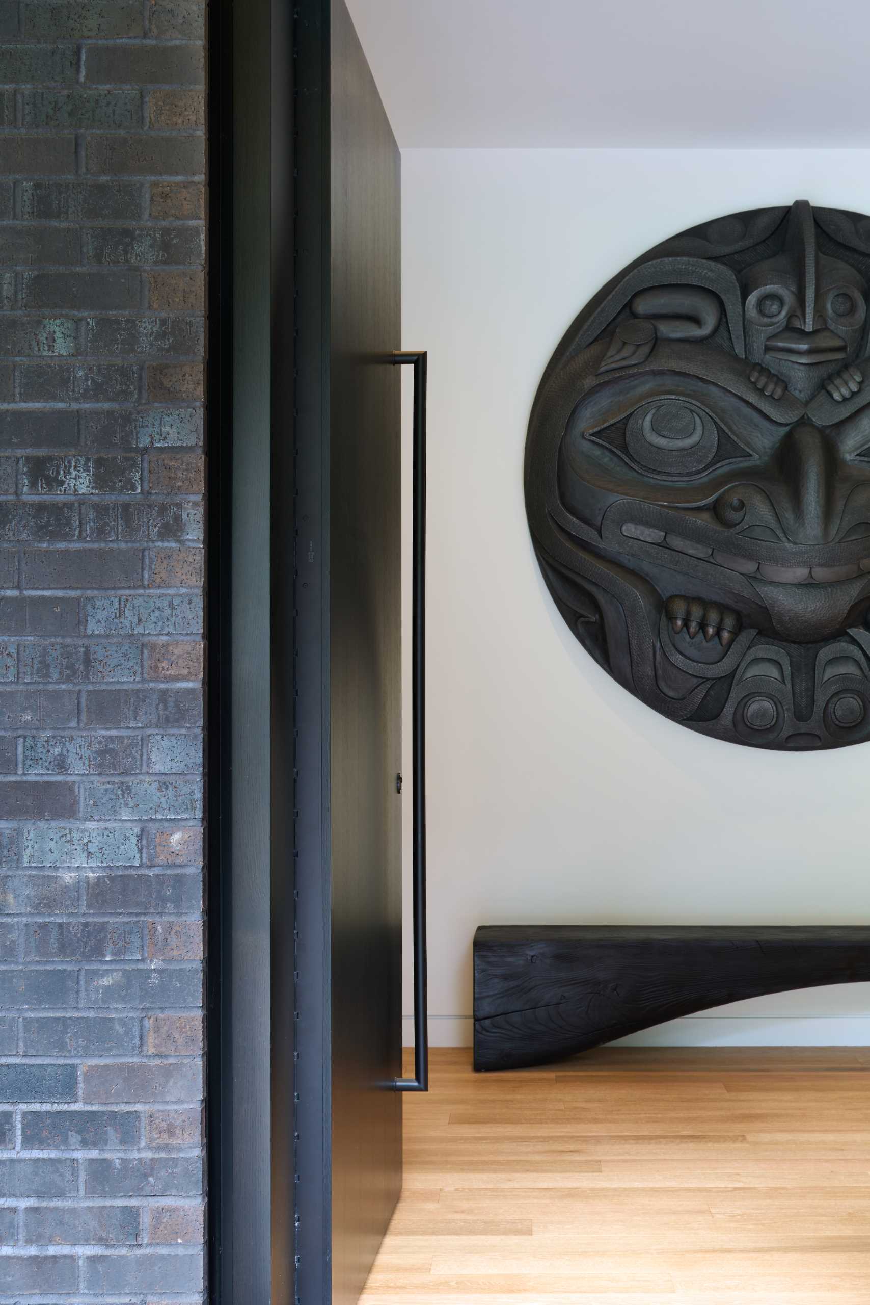 A large and dark front door opens to the entryway with a wall sculpture and bench.