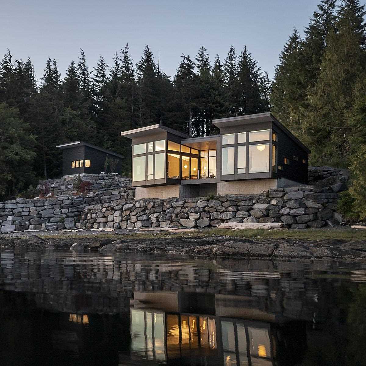 A modern home design has the primary bedroom and living room extend as cantilevers over the rock wall below, giving a sense of floating above the water.