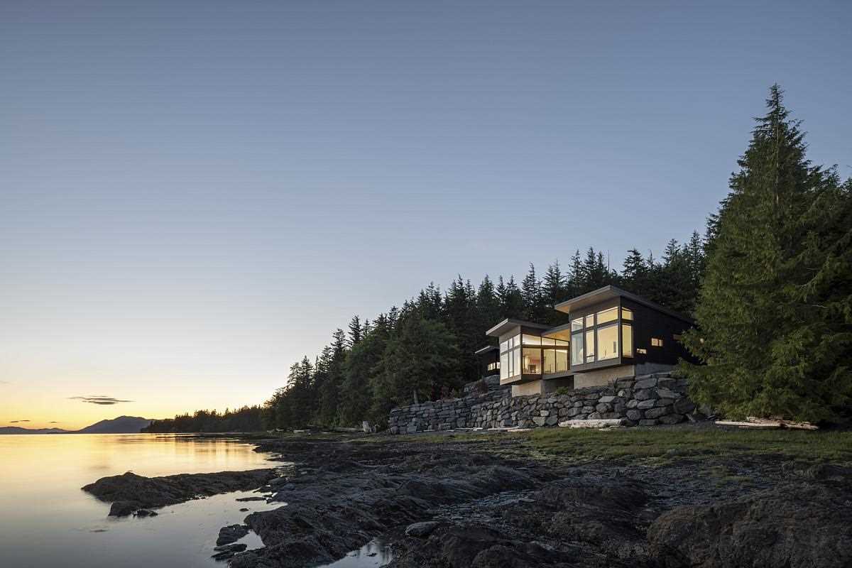 A modern home design has the primary bedroom and living room extend as cantilevers over the rock wall below, giving a sense of floating above the water.