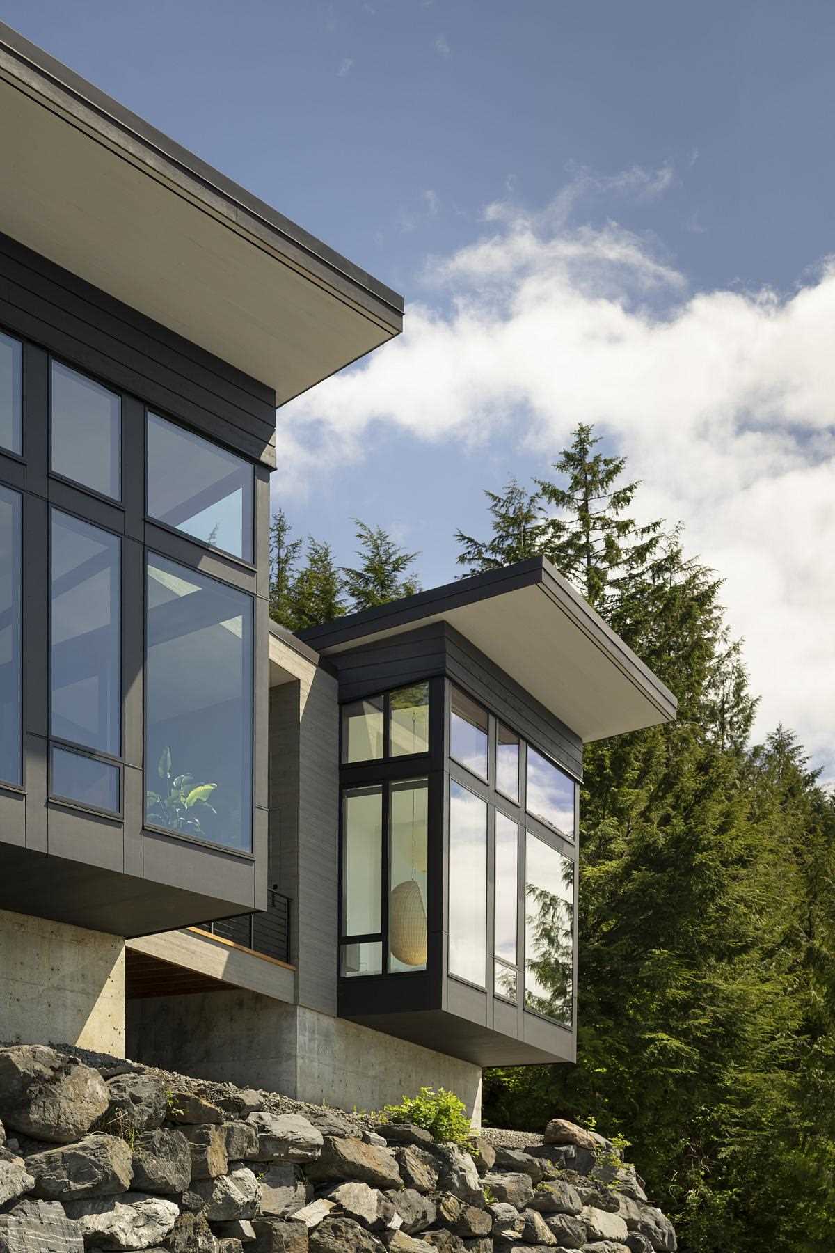 A modern home design has the primary bedroom and living room extend as cantilevers over the rock wall below, giving a sense of floating above the water.