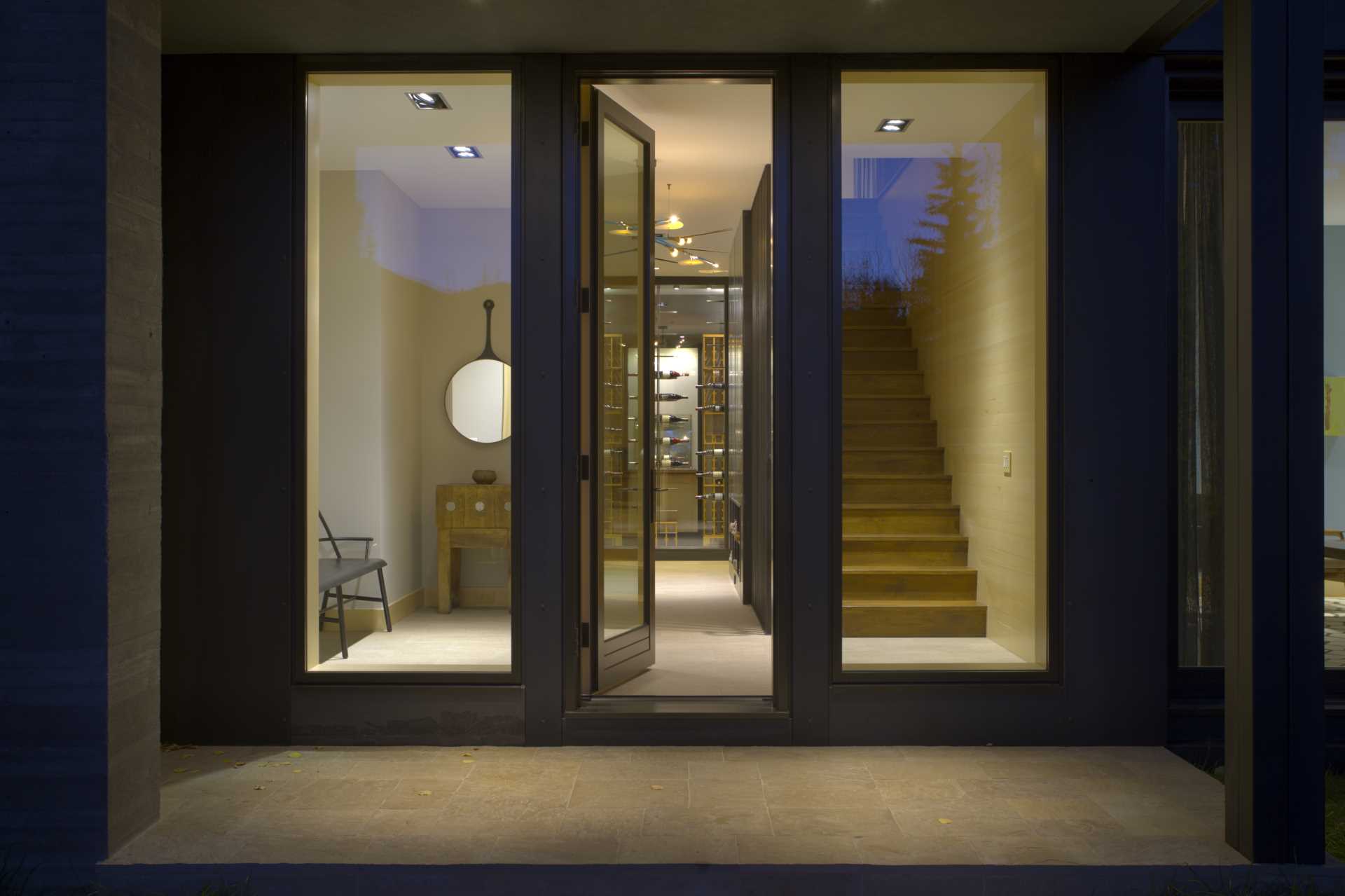 A glass front door welcomes people to the home and provides a view of the entryway, a wine cellar, and stairs.