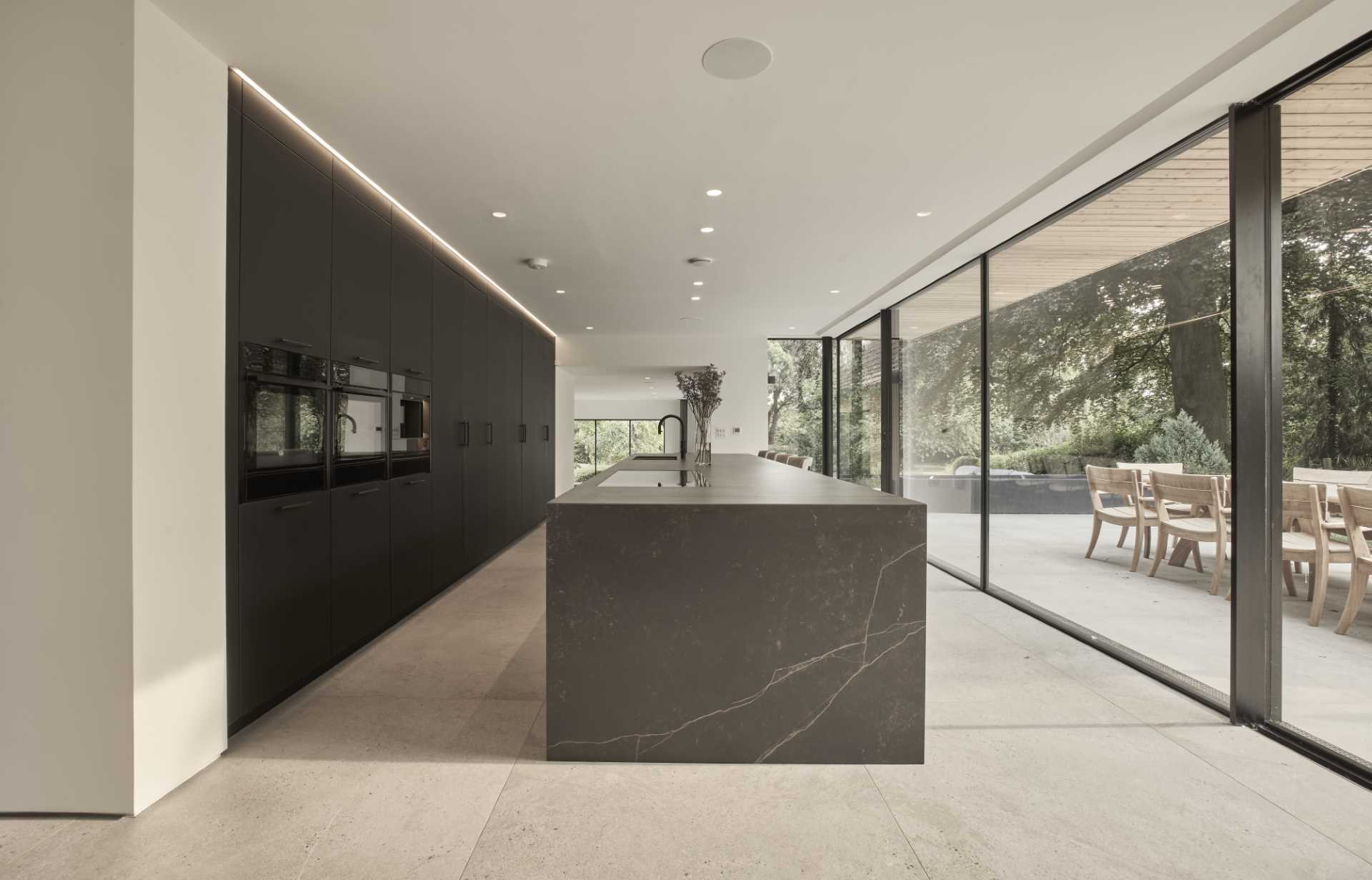 In this modern kitchen, a cleverly concealed pantry, boot room, and utility area are hidden behind the tall cabinetry, accessible through discreet doors that maintain the sleek aesthetic of the space.