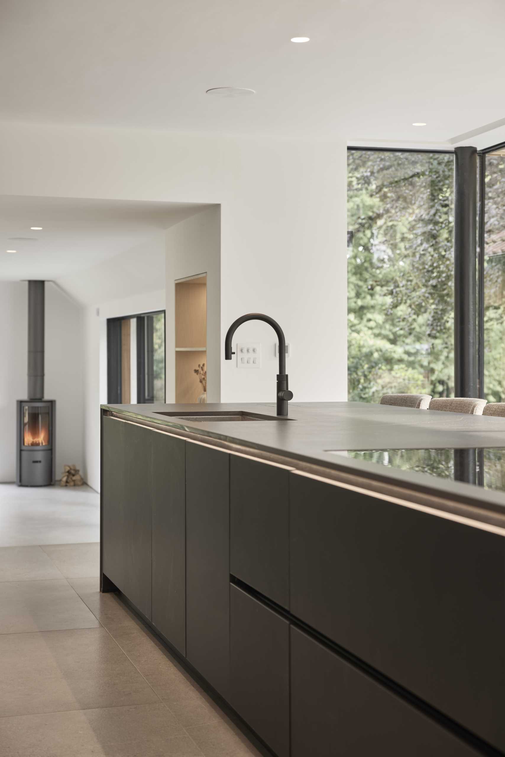 In this modern kitchen, a cleverly concealed pantry, boot room, and utility area are hidden behind the tall cabinetry, accessible through discreet doors that maintain the sleek aesthetic of the space.