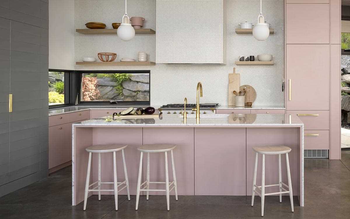 Concrete floors and a concrete hearth wall face pink cabinets and mixed metals in the kitchen. The exhaust hood of the Lacanche Range is wrapped in a mosaic of meticulously placed 1”x1” tiles, helping it to blend into the wall.