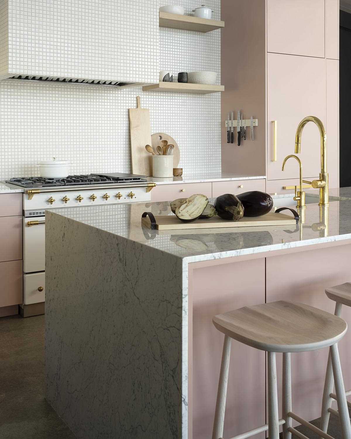 Concrete floors and a concrete hearth wall face pink cabinets and mixed metals in the kitchen. The exhaust hood of the Lacanche Range is wrapped in a mosaic of meticulously placed 1”x1” tiles, helping it to blend into the wall.