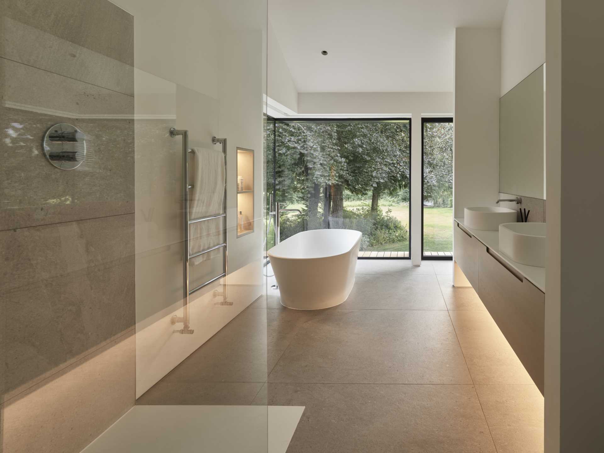 This modern en-suite bathroom becomes a room of serenity, enhanced by large corner window that immerses the space in natural light and offers expansive views of the garden.