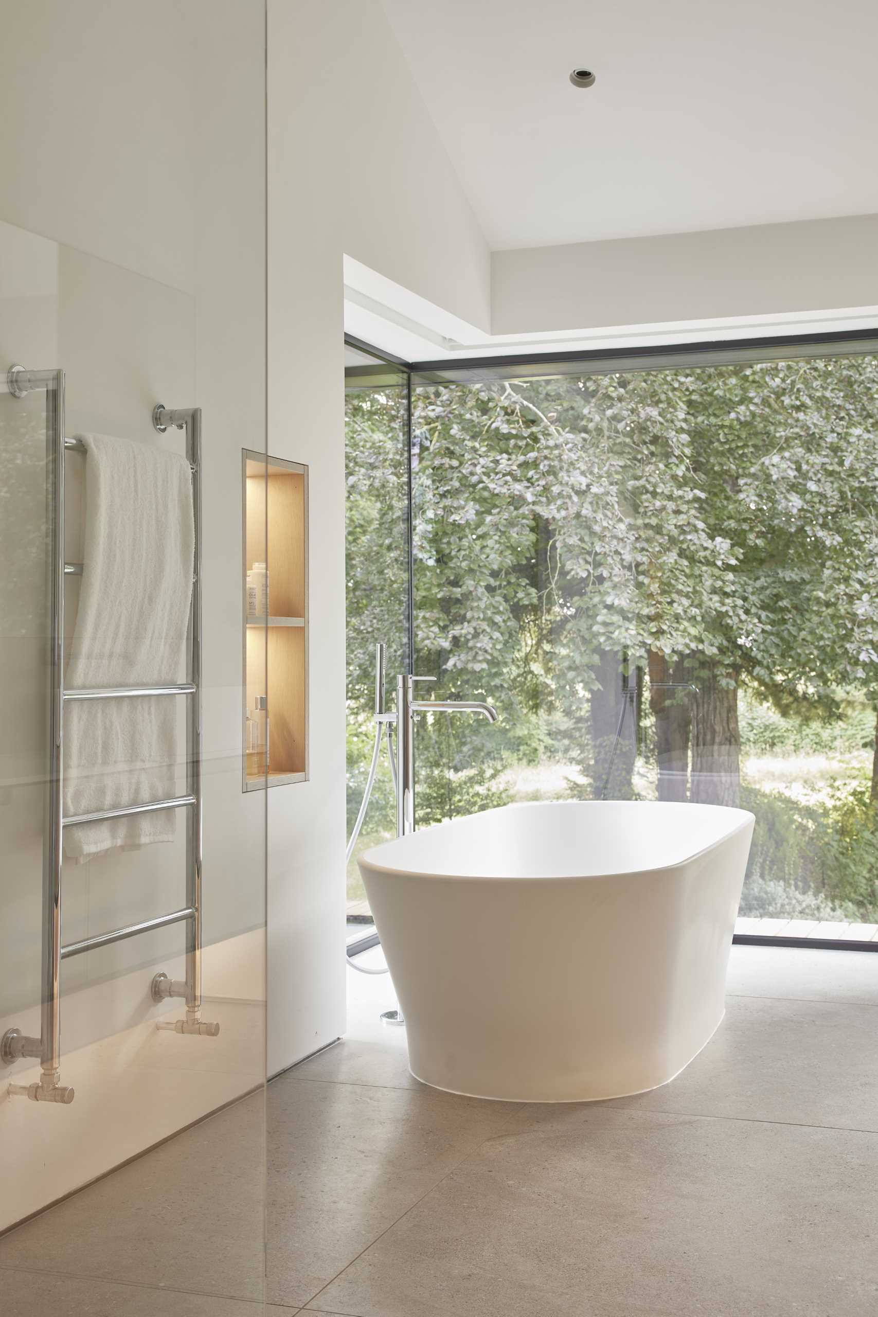 This modern en-suite bathroom becomes a room of serenity, enhanced by large corner window that immerses the space in natural light and offers expansive views of the garden.