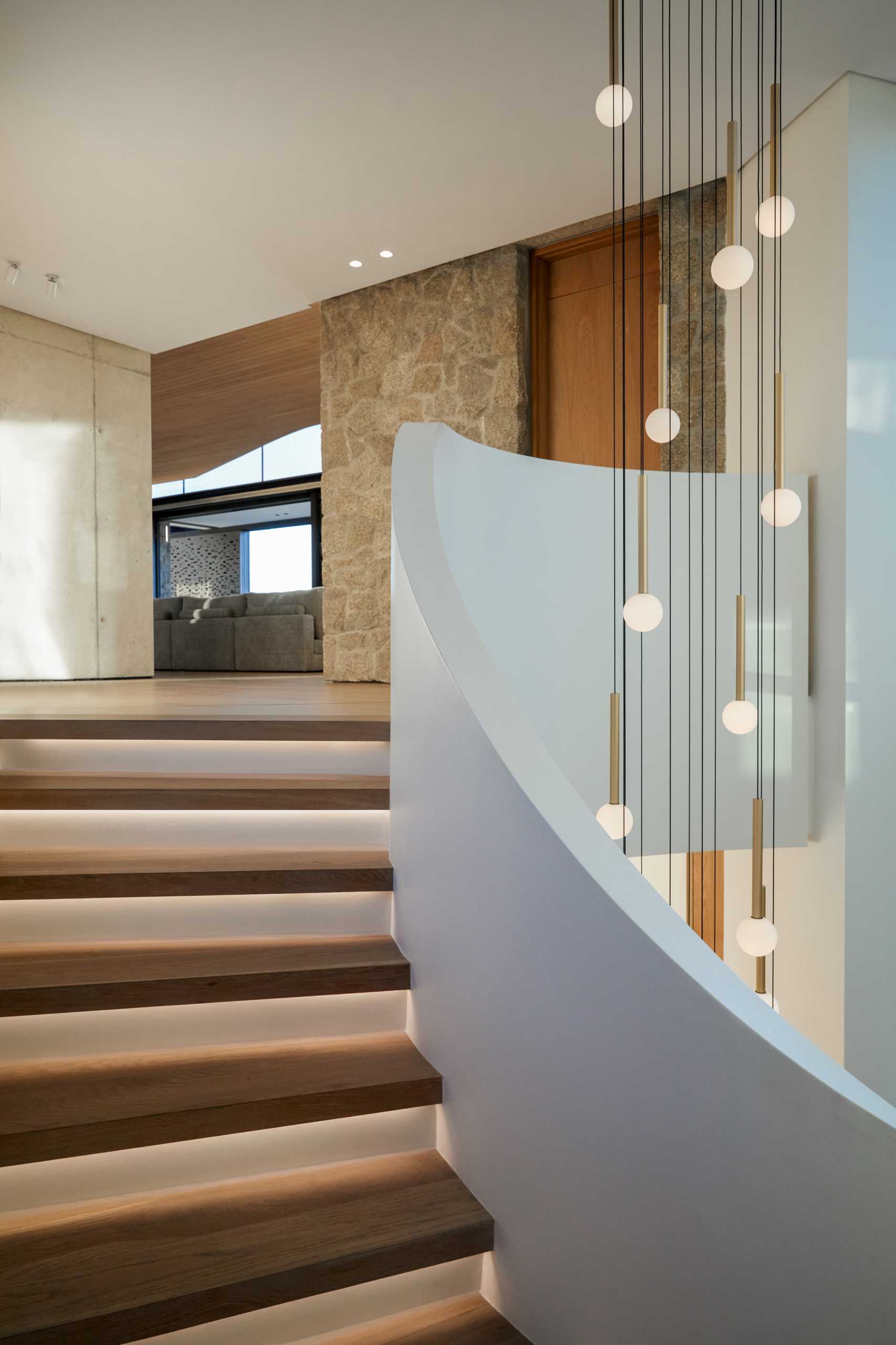 A modern home with a sculptural staircase that also includes pendant lights at varying heights, as well as hidden lighting underneath the treads.