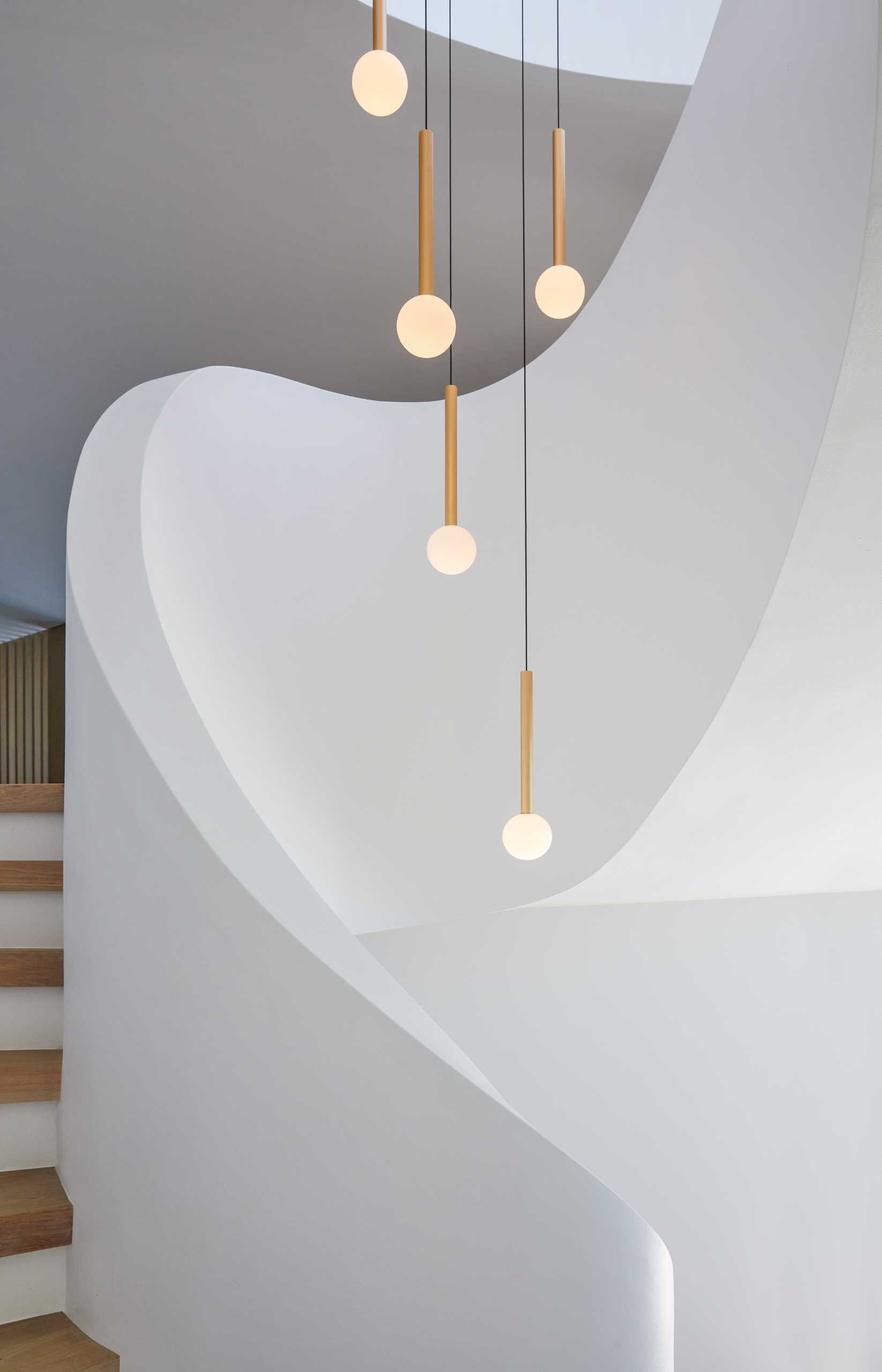 A modern home with a sculptural staircase that also includes pendant lights at varying heights.