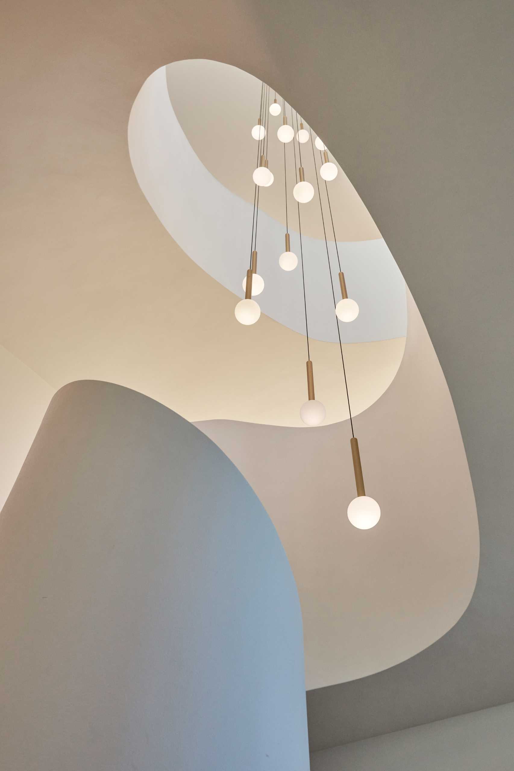 A modern home with a sculptural staircase that also includes pendant lights at varying heights.