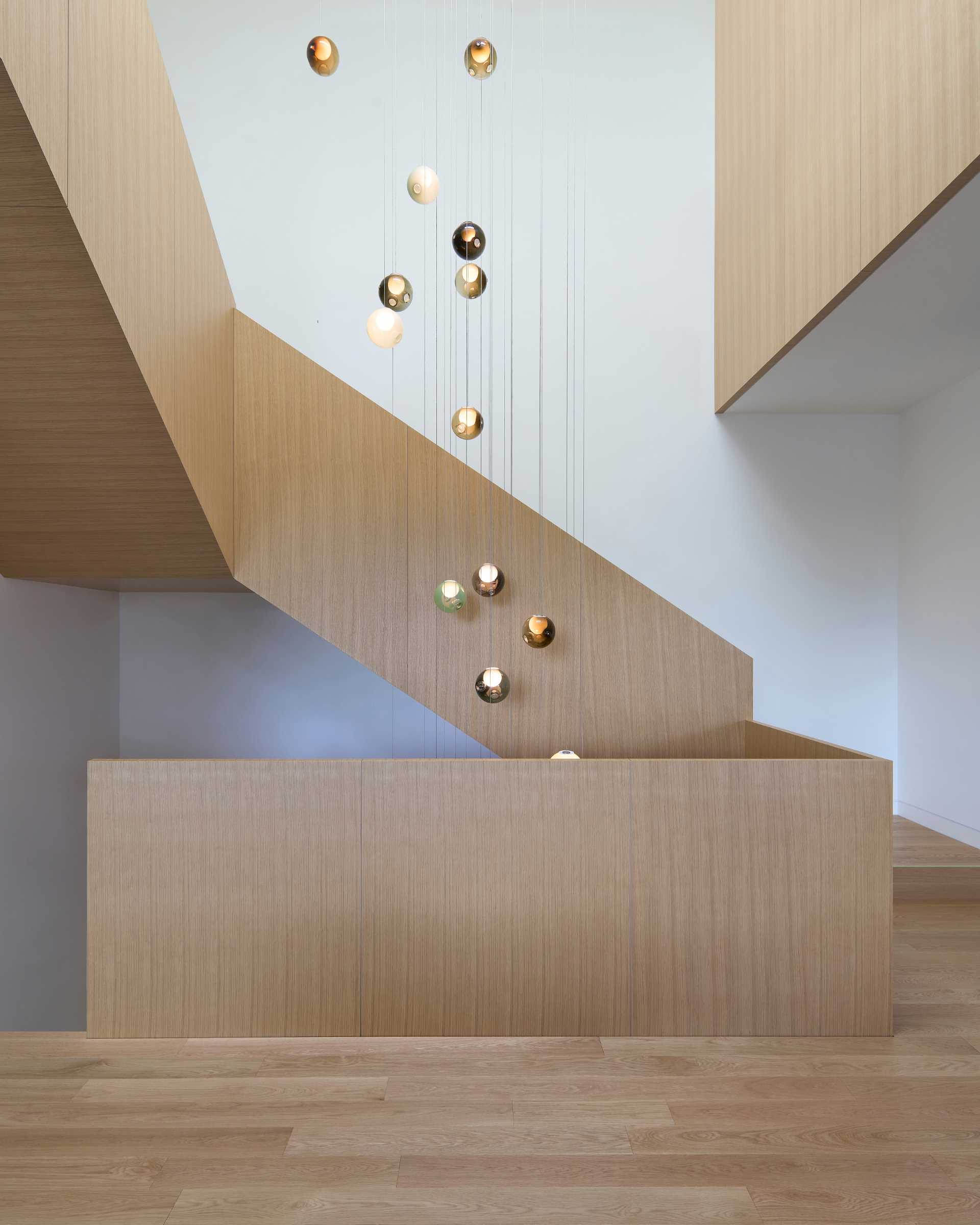 A standout architectural feature in this modern home is the grand oak staircase, which spirals around a suspended three-story glass chandelier.