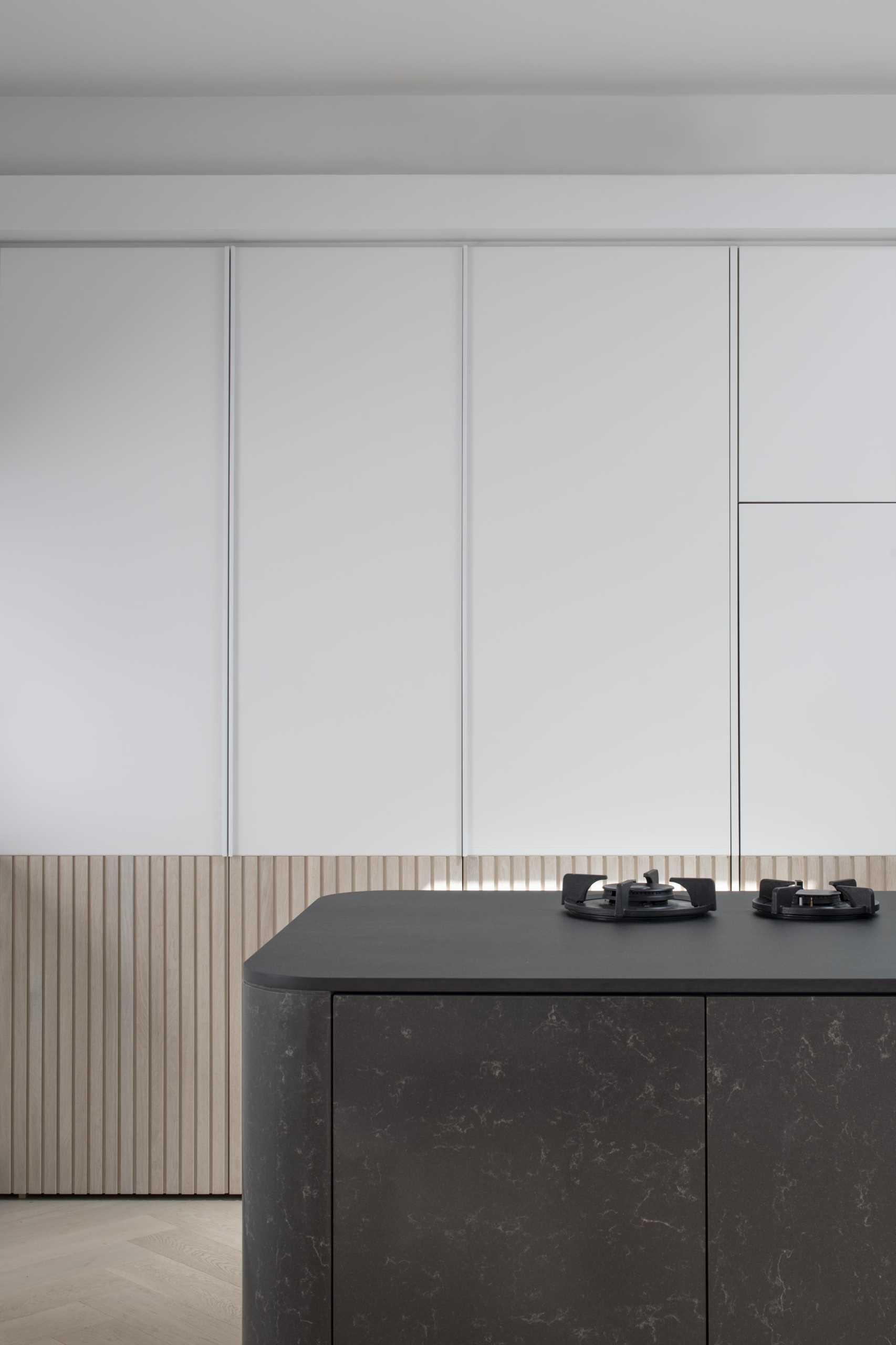 A modern white kitchen with wood paneling around the lower section of the cabinets. Integrated appliances have also been included in the kitchen design.