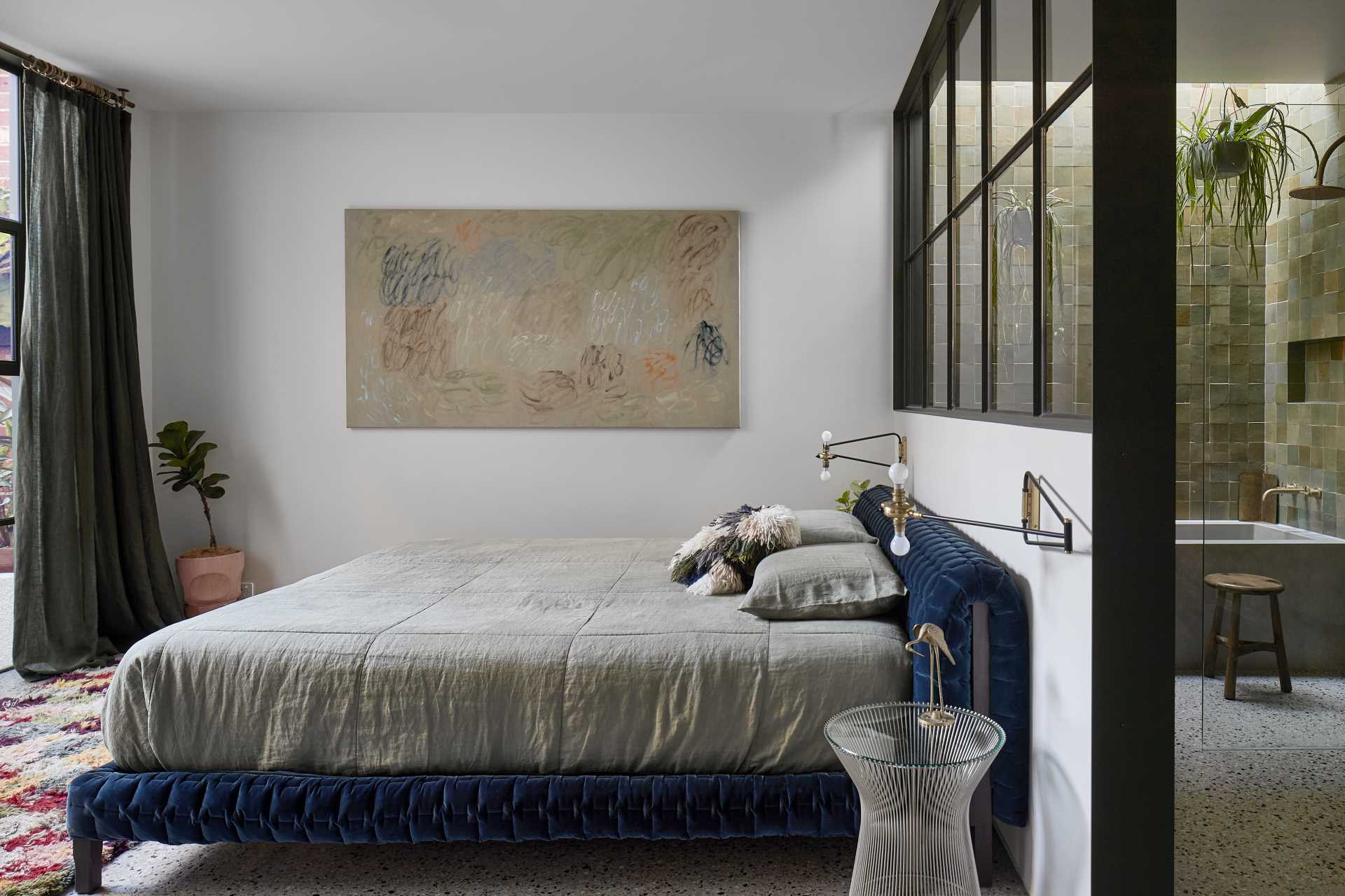 This modern main bedroom suite features a private landscaped courtyard, while a full-width steel window separates the bedroom from the green-drenched walls of handmade Spanish tiles and hanging plants in the en-suite bathroom.