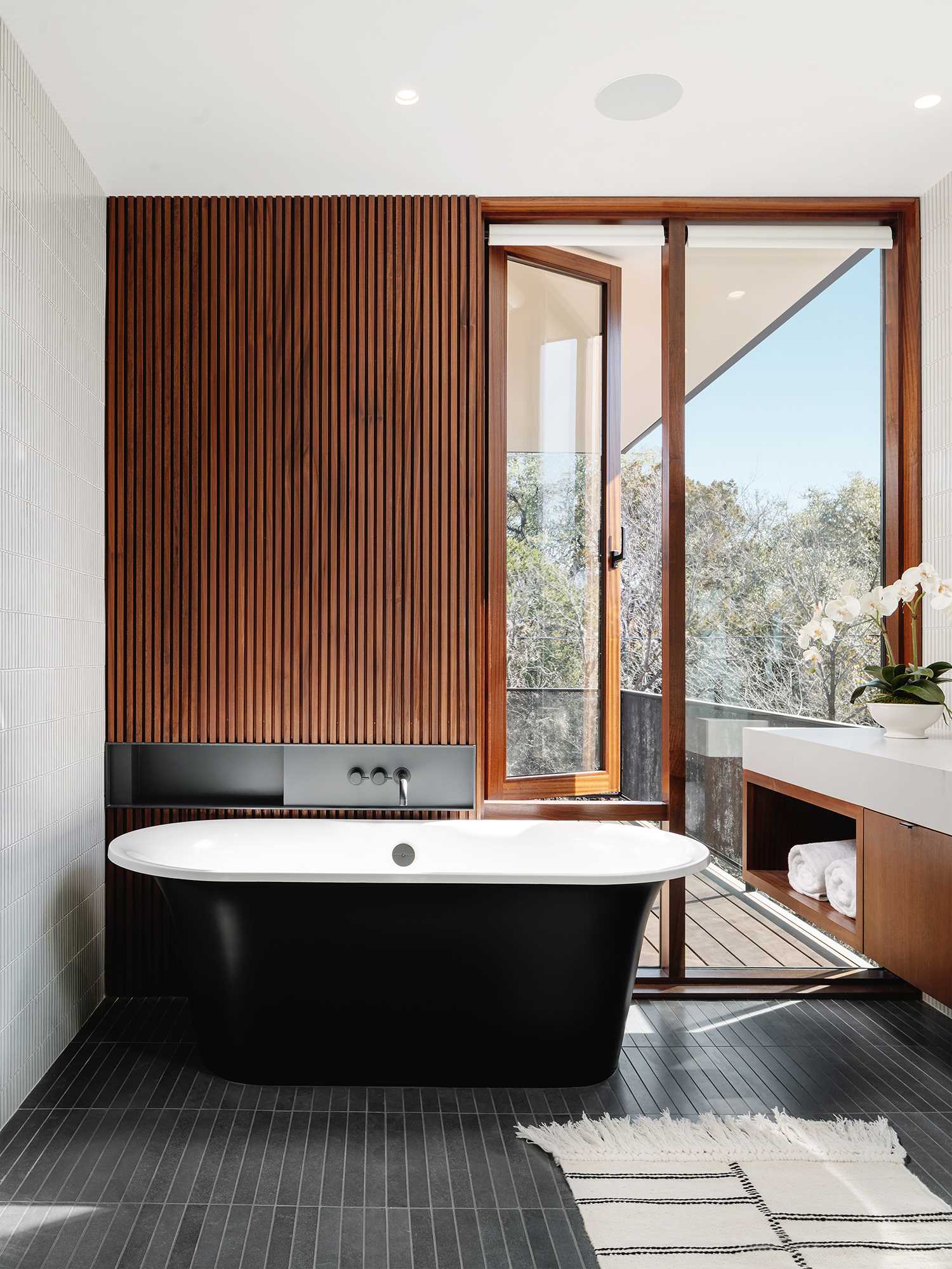 A modern bathroom with tile-clad walls and floor, a long double vanity, and a freestanding bathtub.