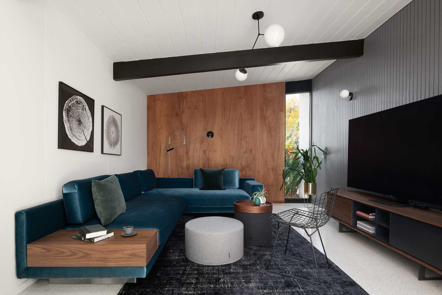 A mid-century inspired living room with a blue velvet couch, a grey accent wall, and wood elements that complement the other wood elements found throughout the home.