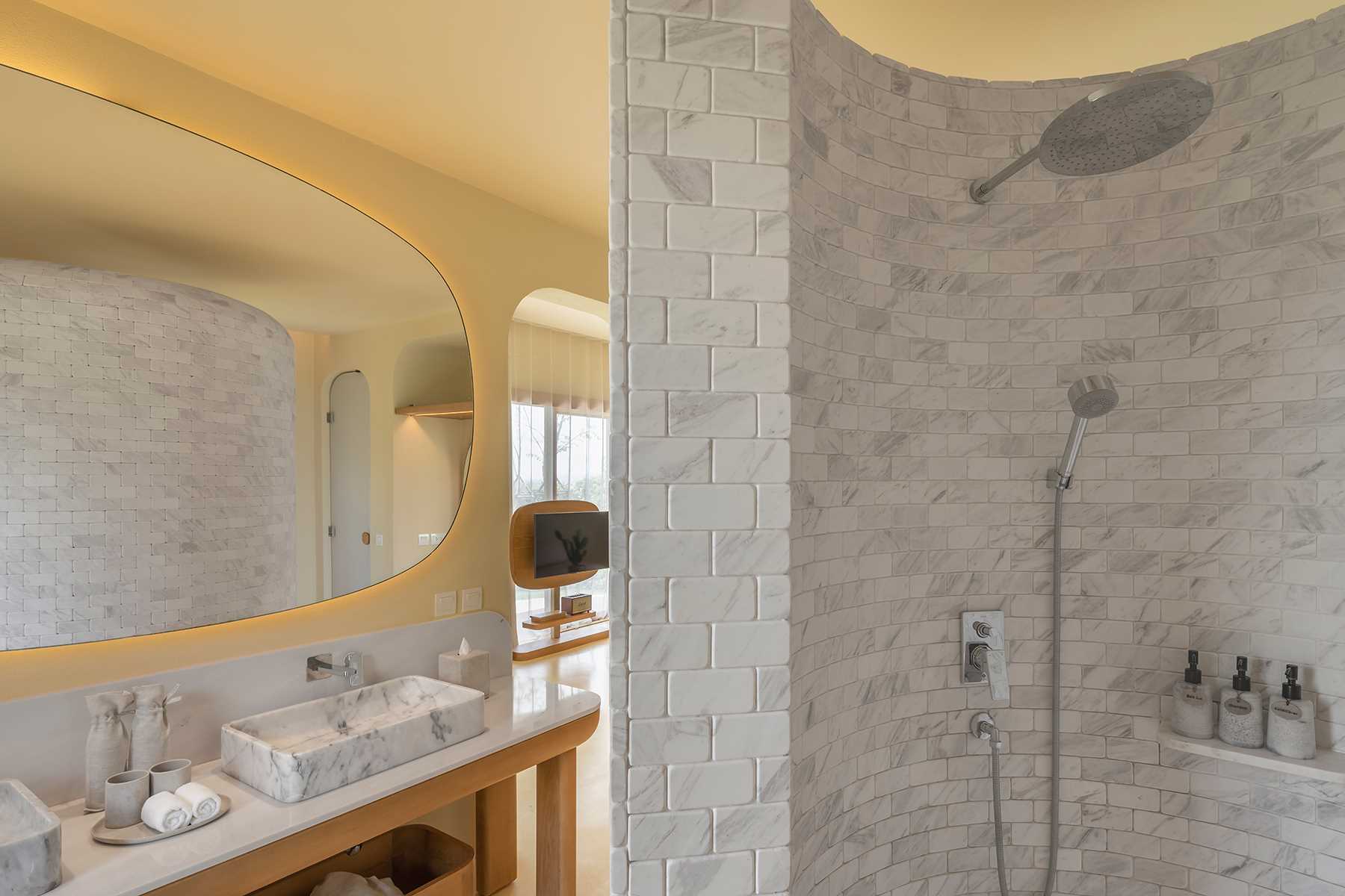 A modern bathroom with earth tones and a curved marble clad shower wall.