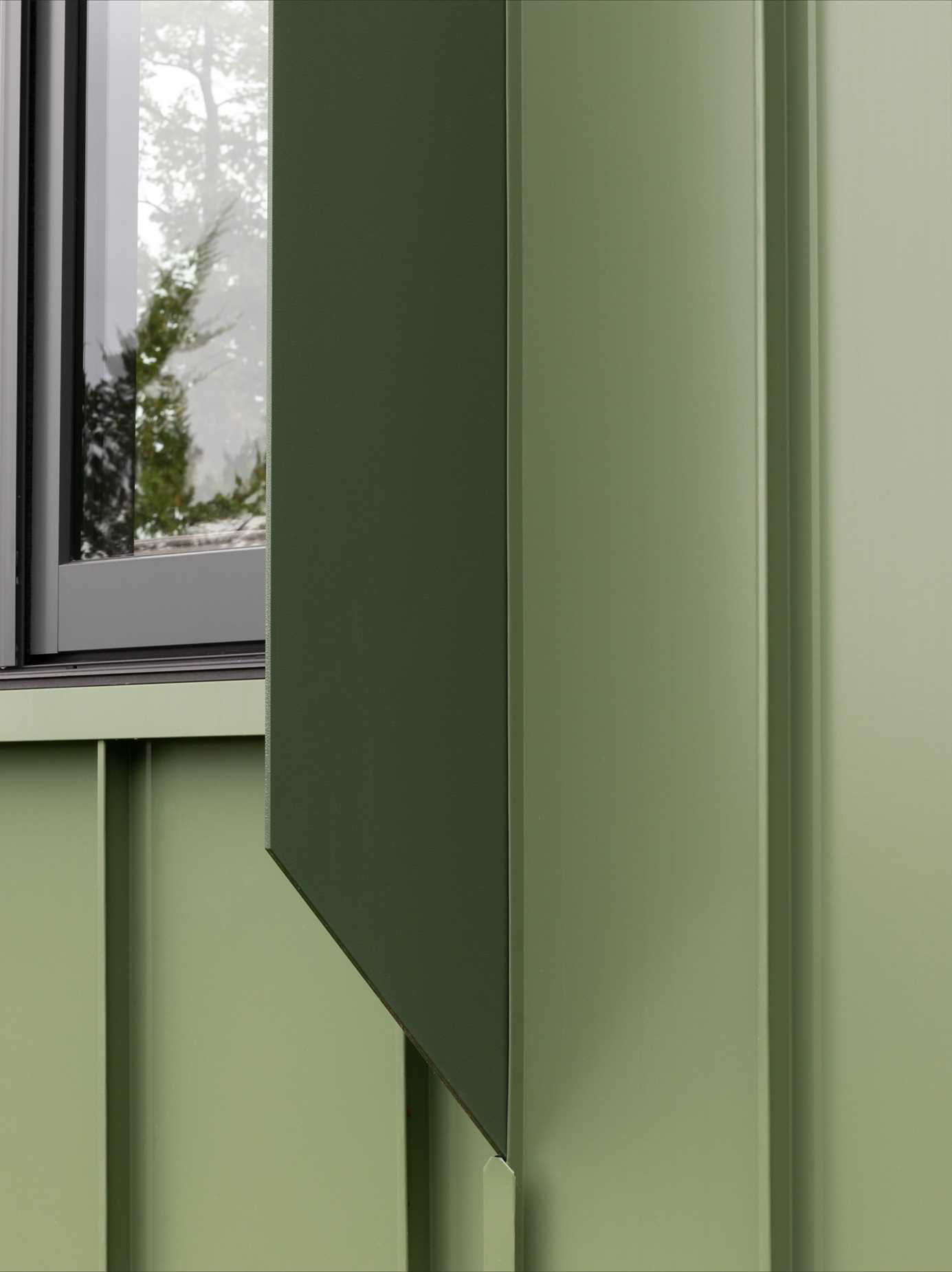 A modern cabin clad in sage green standing seam metal siding.