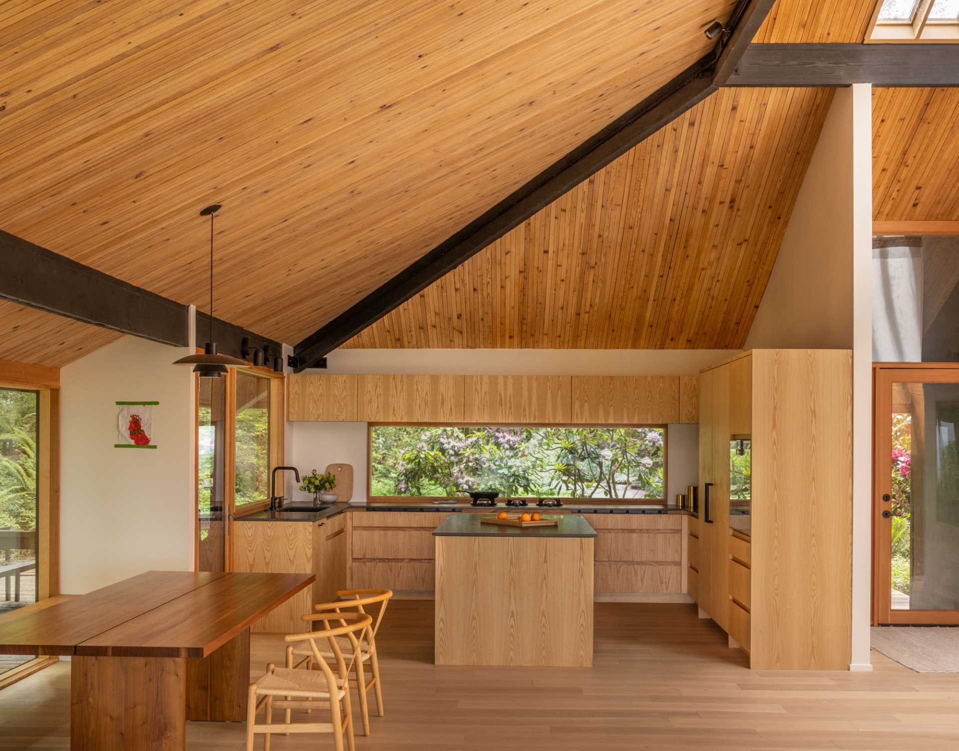 The kitchen includes a horizontal window above the cooktop, offering views of mature rhododendrons, as well as plain-sawn Ash cabinetry and Basaltina Natural Stone countertop with a honed finish.