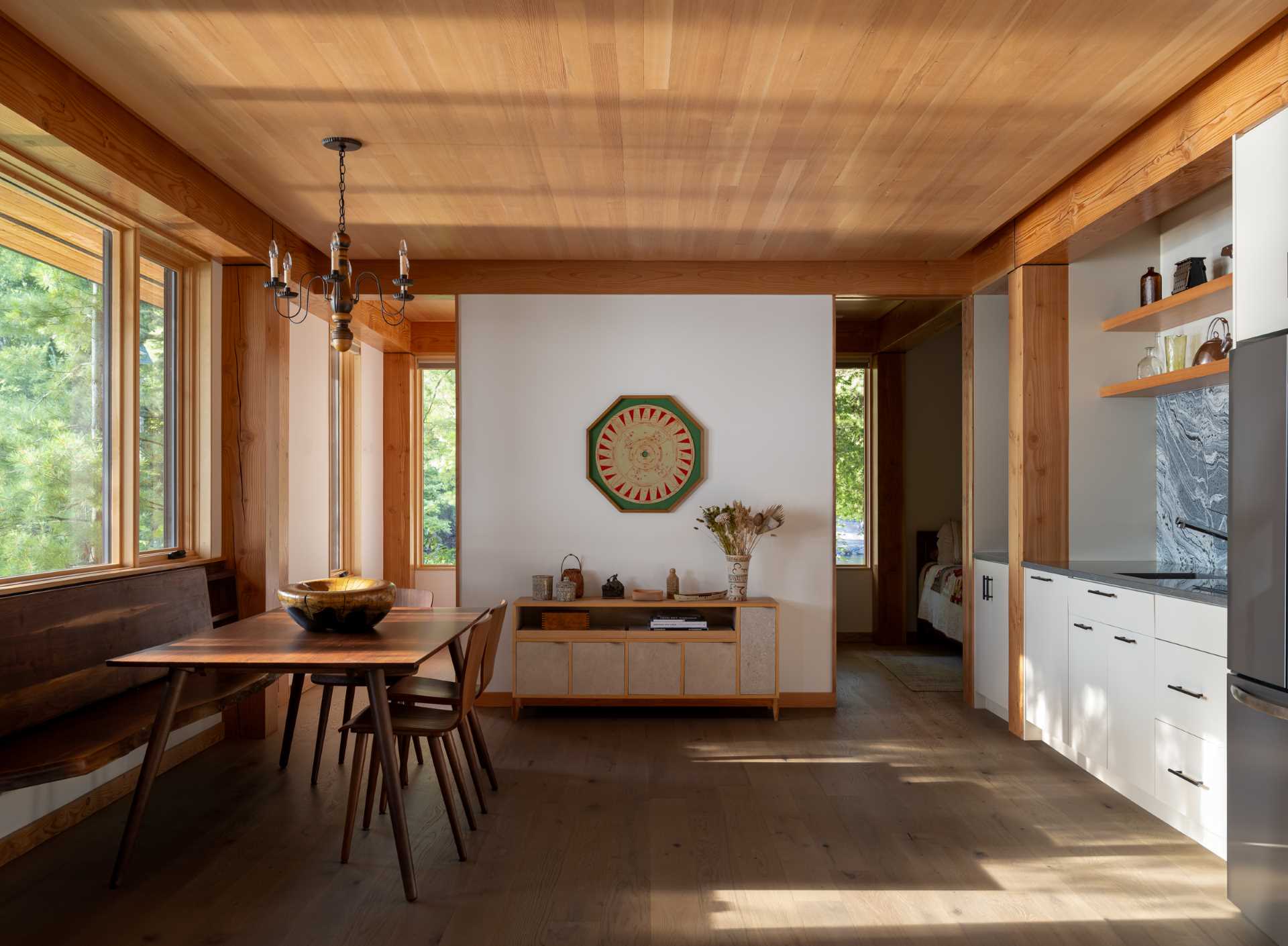 The dining area of this small cabin includes a wood bench that runs underneath the window, while the kitchen takes up the opposite wall.