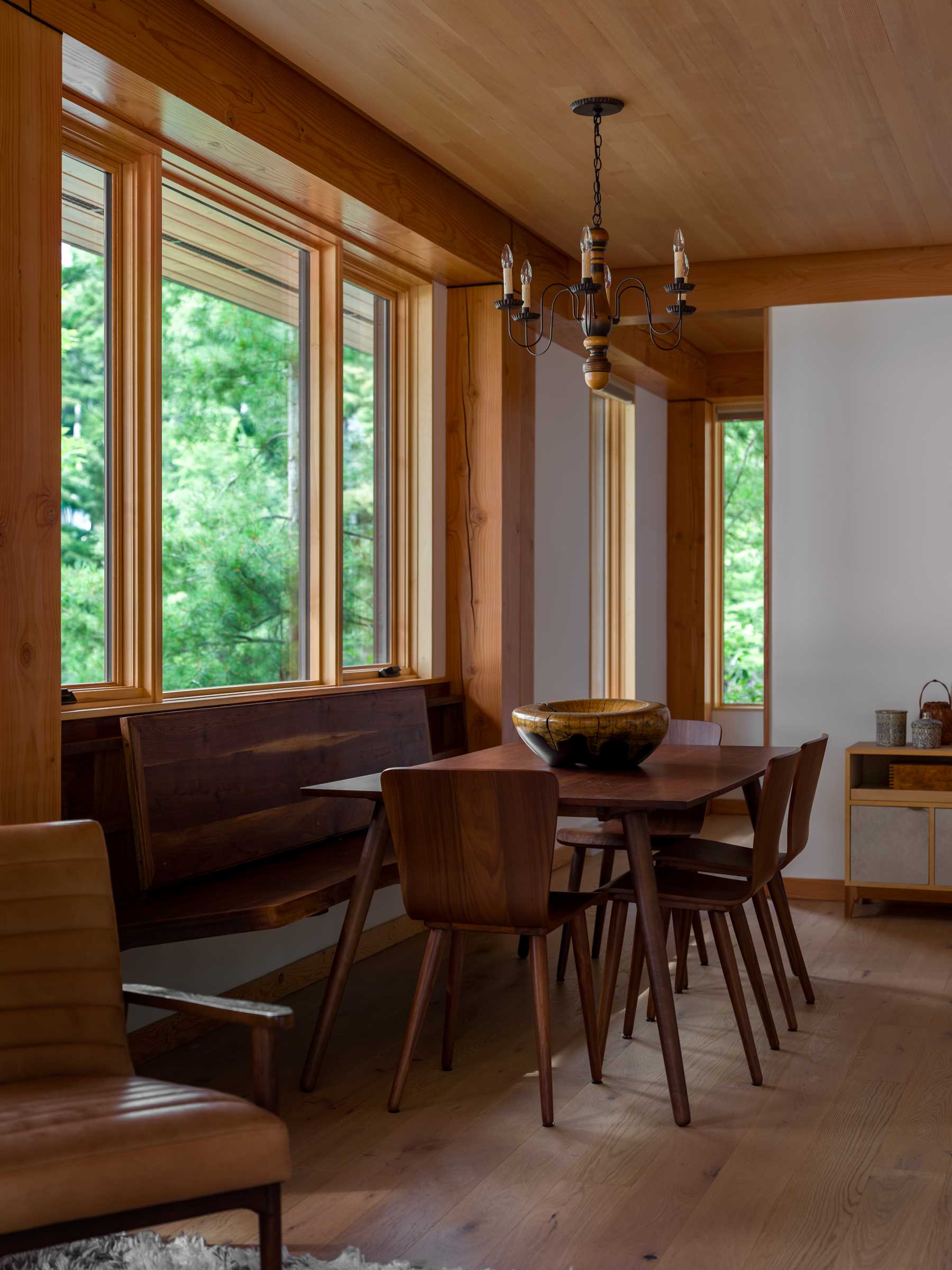 The dining area of this small cabin includes a wood bench that runs underneath the window, while the kitchen takes up the opposite wall.