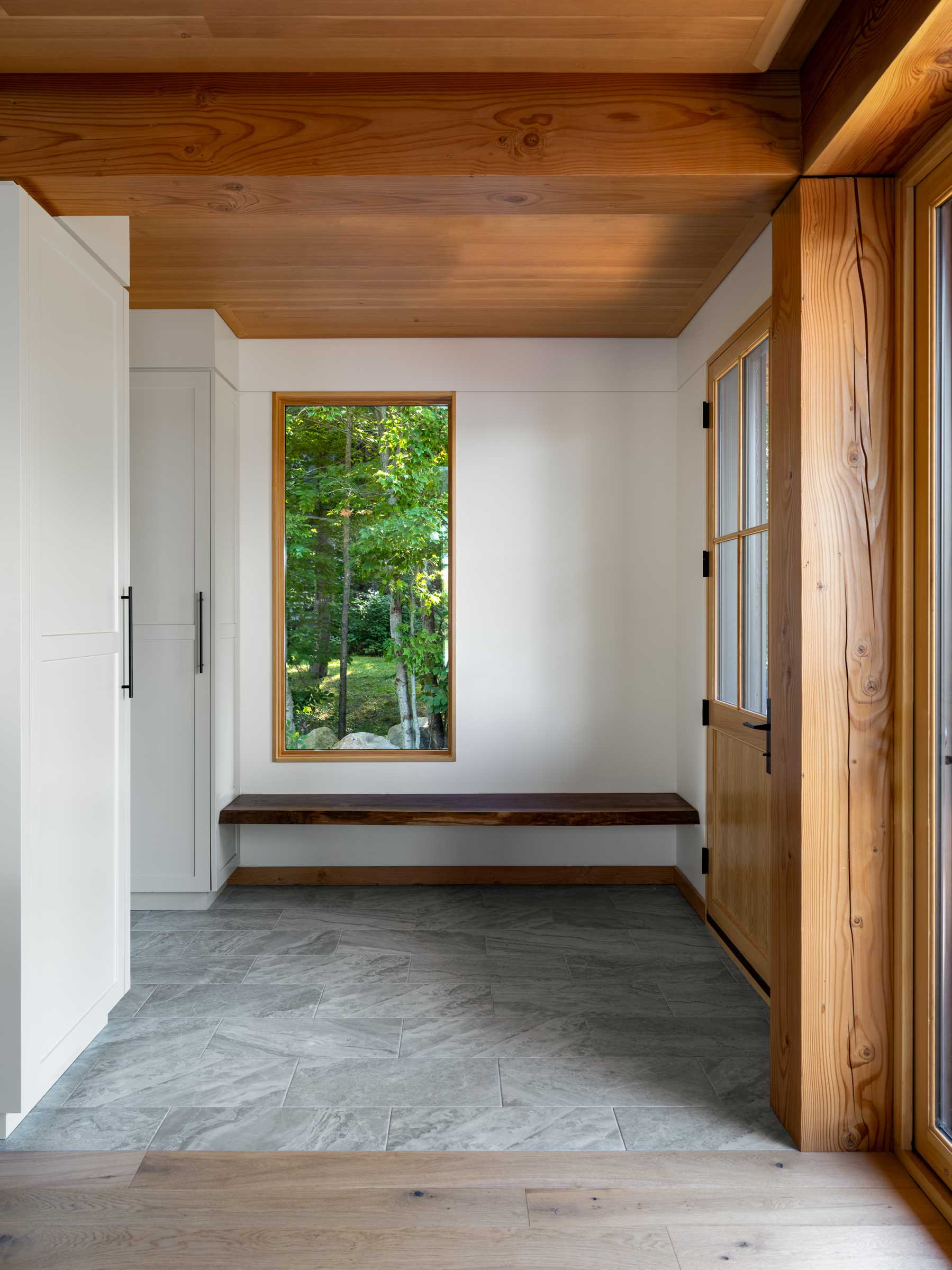 An entryway with a floating wood bench, and a window that perfectly frames the trees outside, replacing the need for artwork.