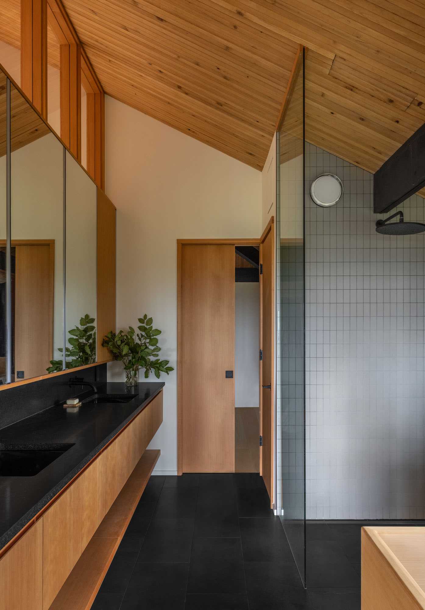 This primary bathroom has natural stone "Basalto" tiles on the floor and an Absolute Black Antiqued Granite countertop with a custom wood vanity. In the shower, there's a contemporary 12" round rainhead and stacked mosaic Ann Sacks tiles in a Foundry matte color.