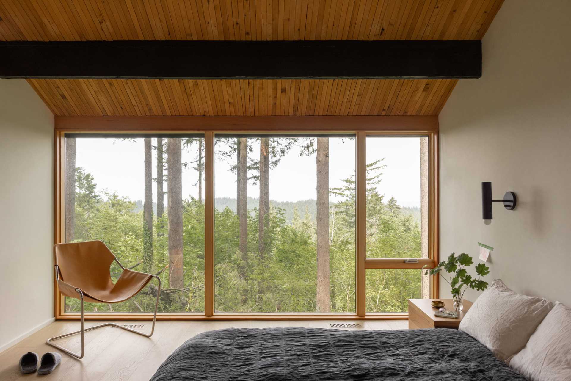 In this primary bedroom, floor-to-ceiling windows provide an uninterrupted view of the trees.