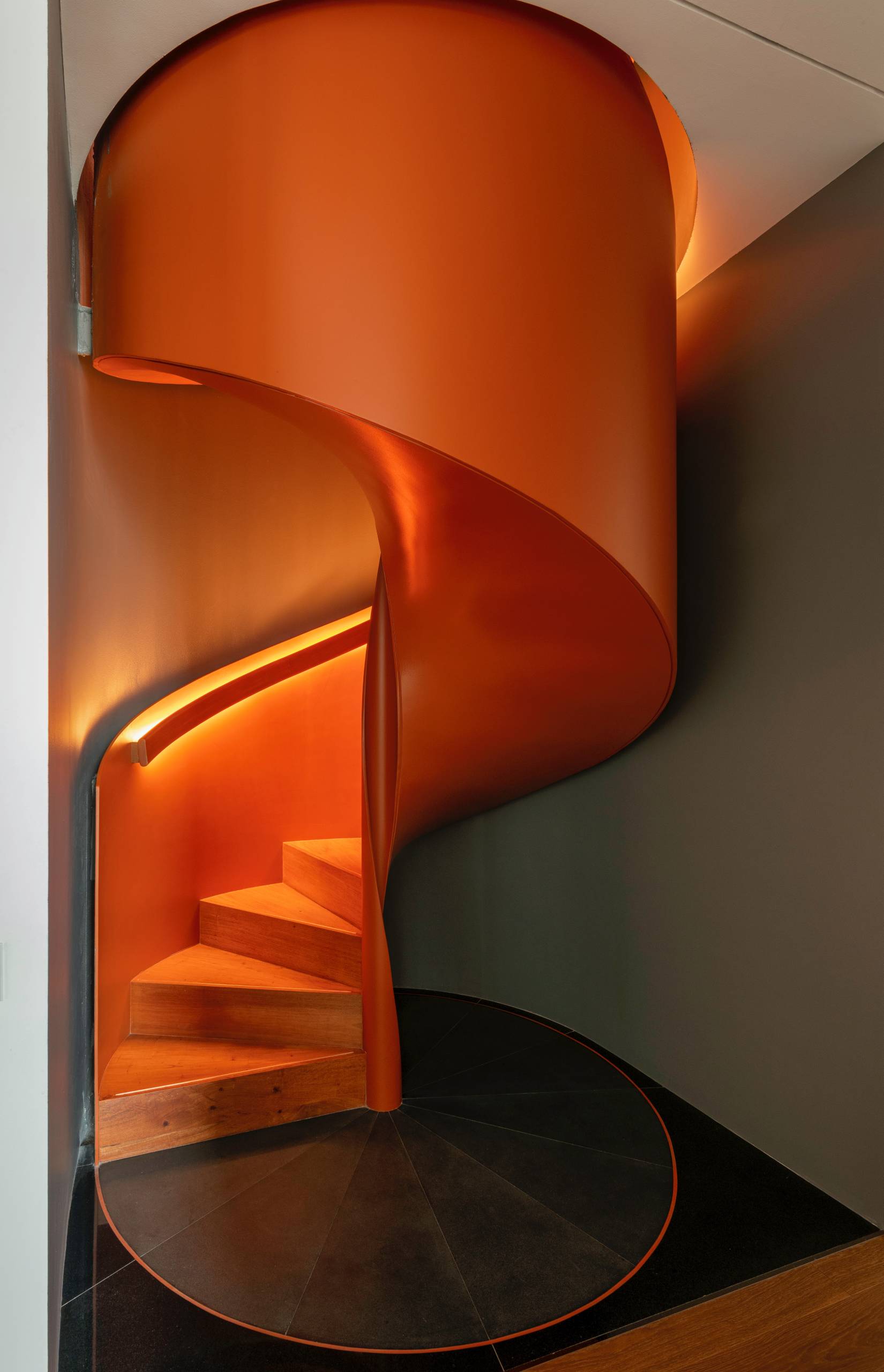 A modern penthouse with a bright orange spiral staircase.