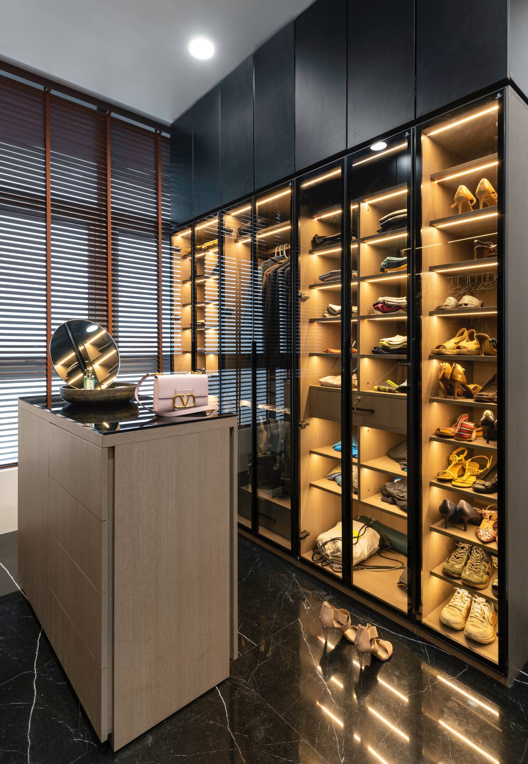 A walk-in closet with shelving that has lights to highlight the clothing and shoes.