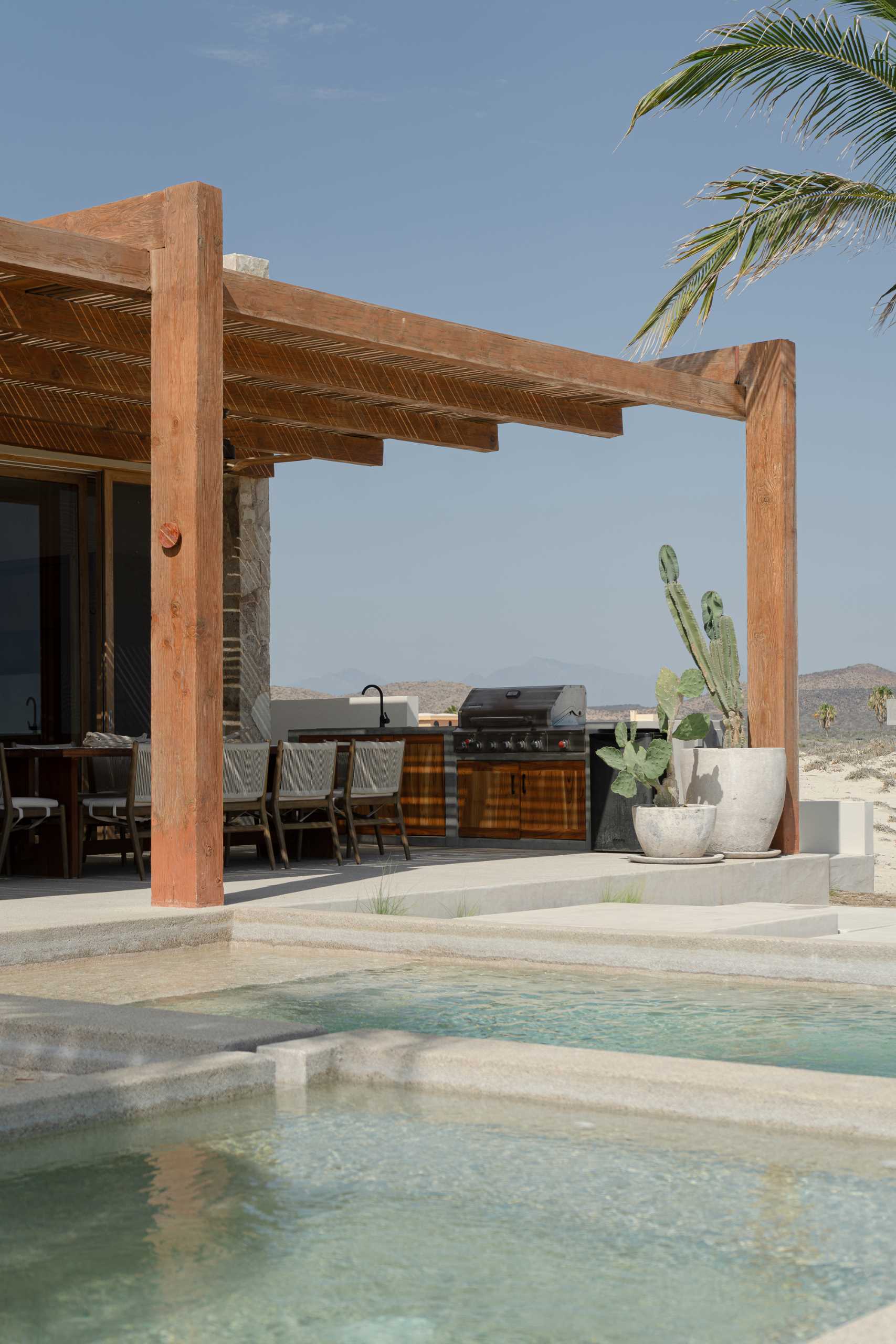 A contemporary stone home includes a spacious terrace, as well as a series of sculptural concrete cubes that form the pool and jacuzzi, while steps lead directly to the sand.