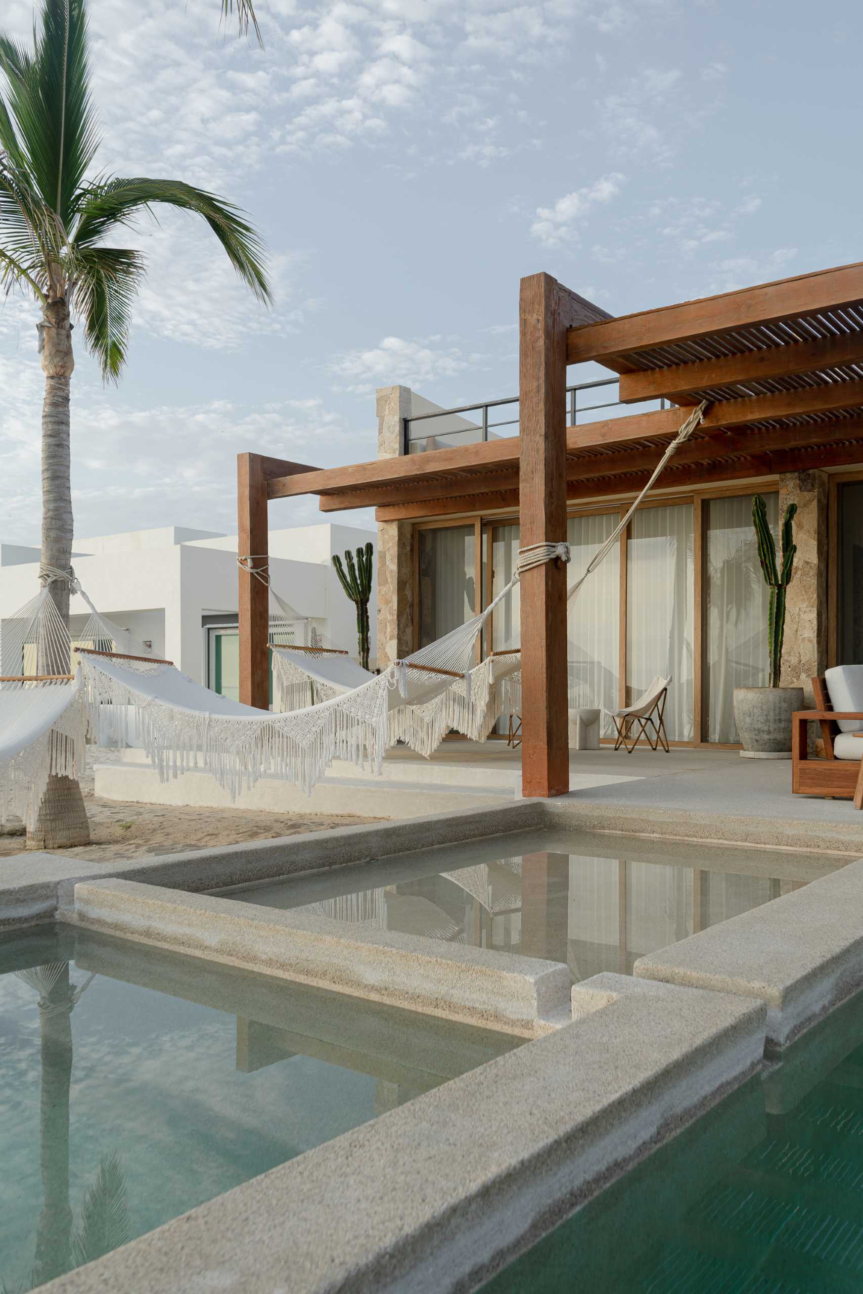 A contemporary stone home includes a spacious terrace, as well as a series of sculptural concrete cubes that form the pool and jacuzzi, while steps lead directly to the sand.