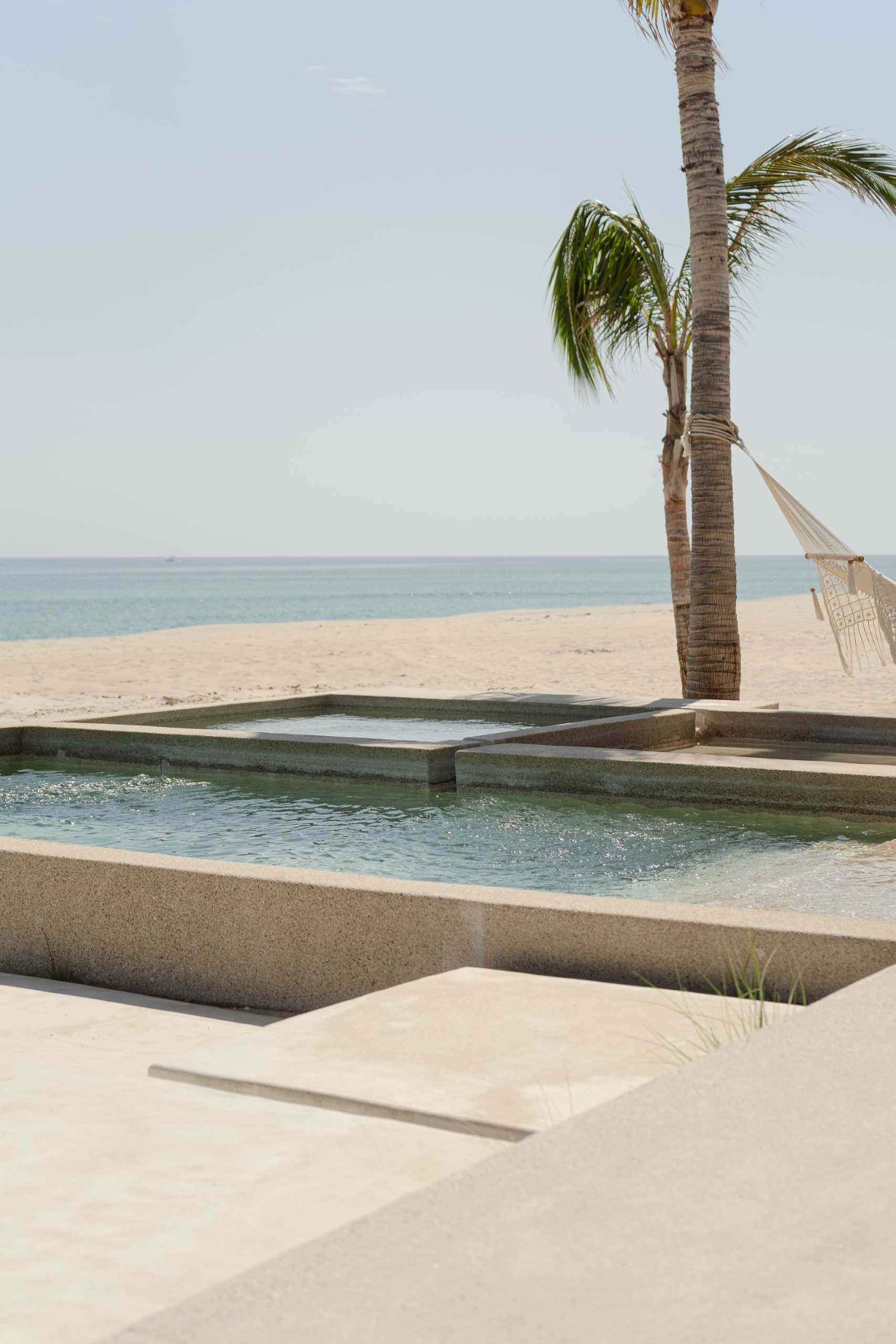 A contemporary stone home includes a spacious terrace, as well as a series of sculptural concrete cubes that form the pool and jacuzzi, while steps lead directly to the sand.