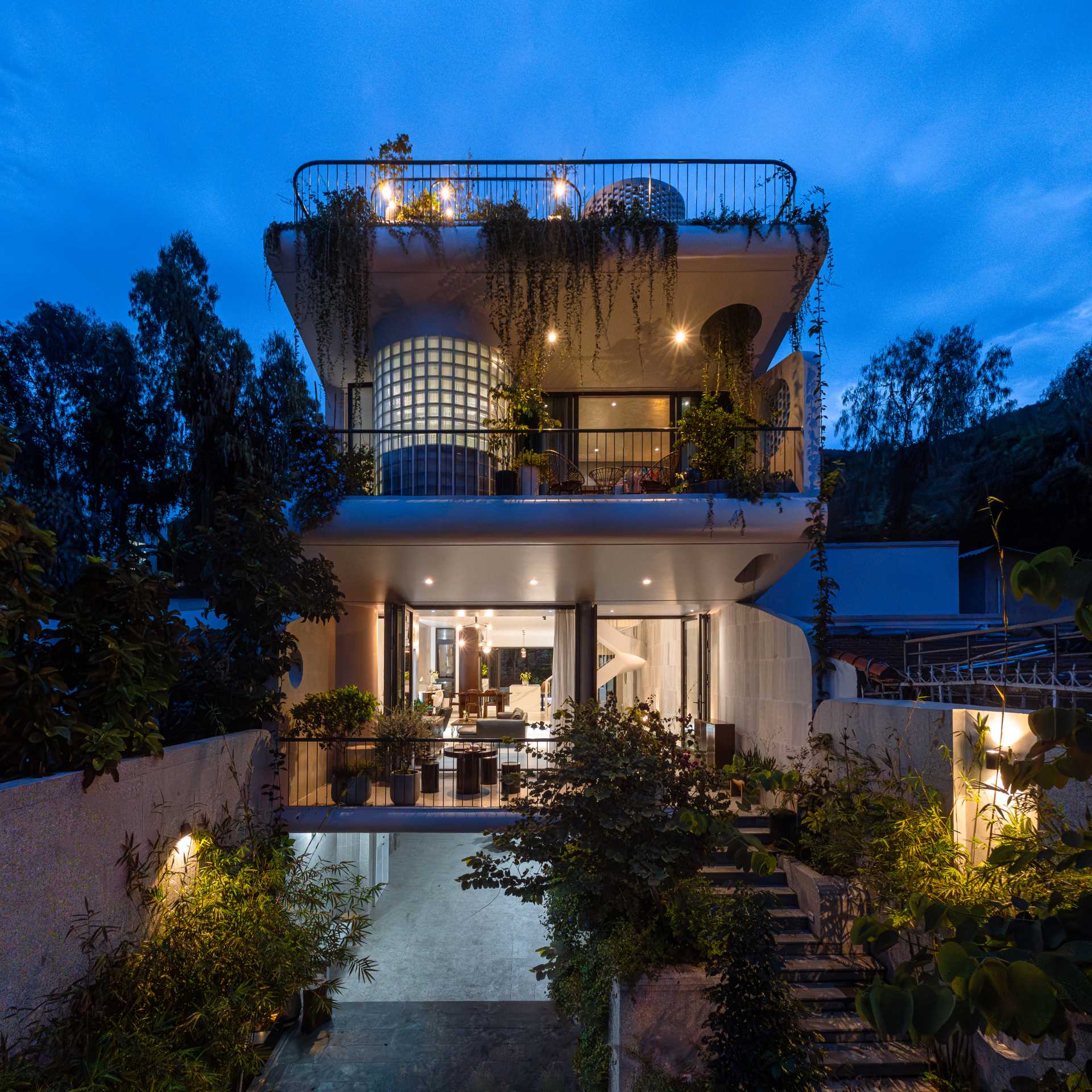 At night, exterior lighting highlights the various design elements of the home, like the plants, glass blocks, or the soft curved architectural volumes.