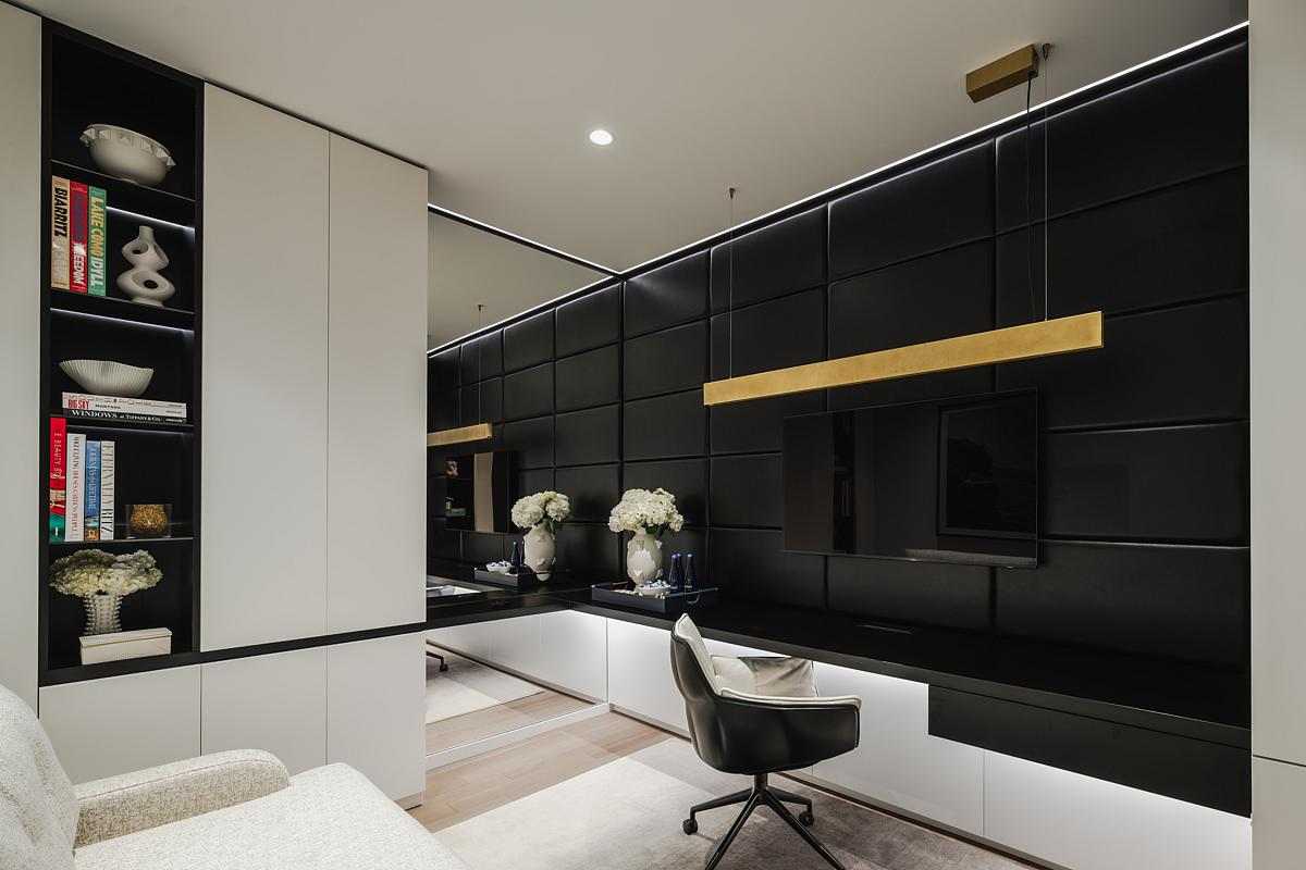 The interior design of a home office. with a couch, built-in desk, textured black leather panels, a mirrored wall, and plenty of storage cabinets.