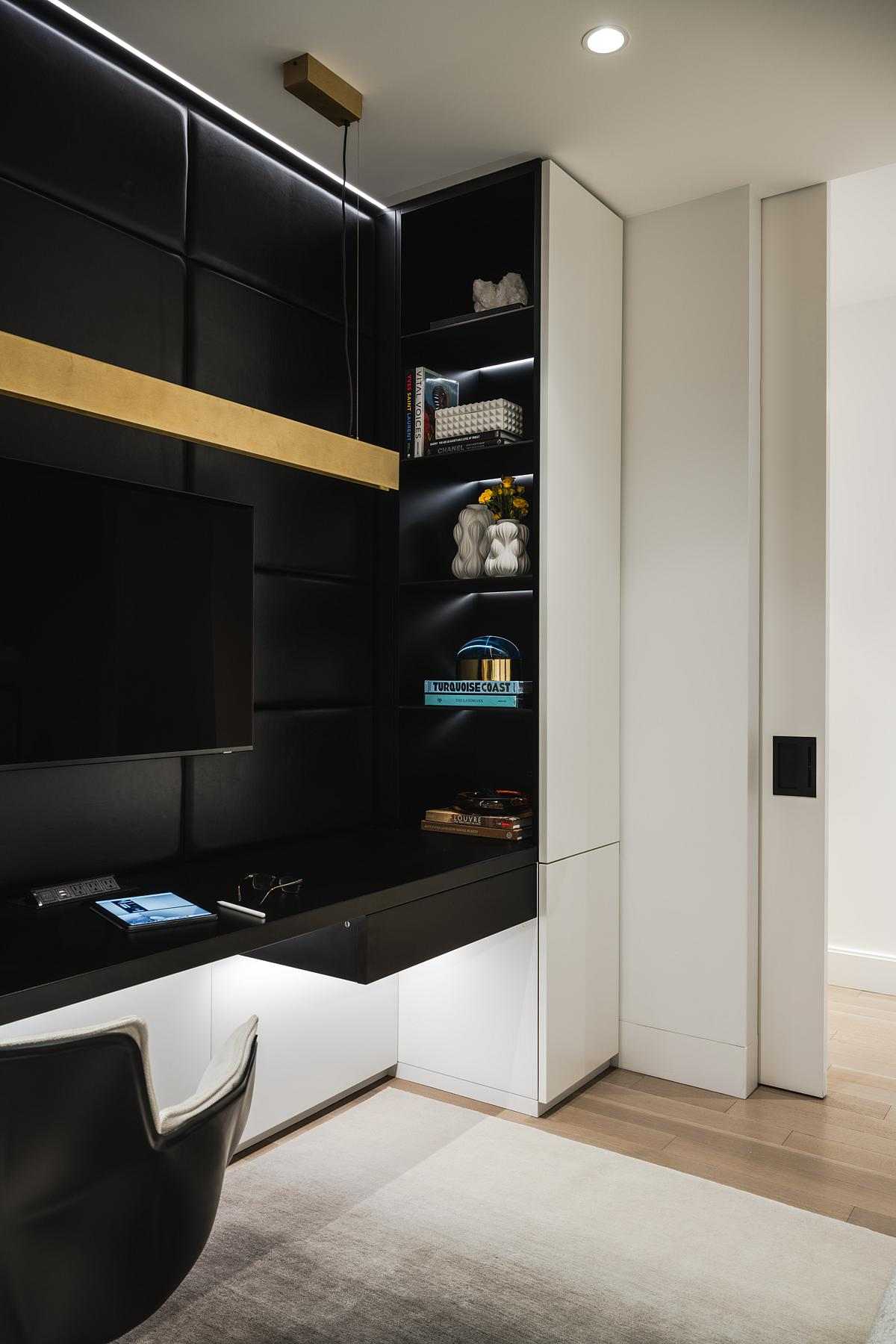 The interior design of a home office. with a couch, built-in desk, textured black leather panels, a mirrored wall, and plenty of storage cabinets.