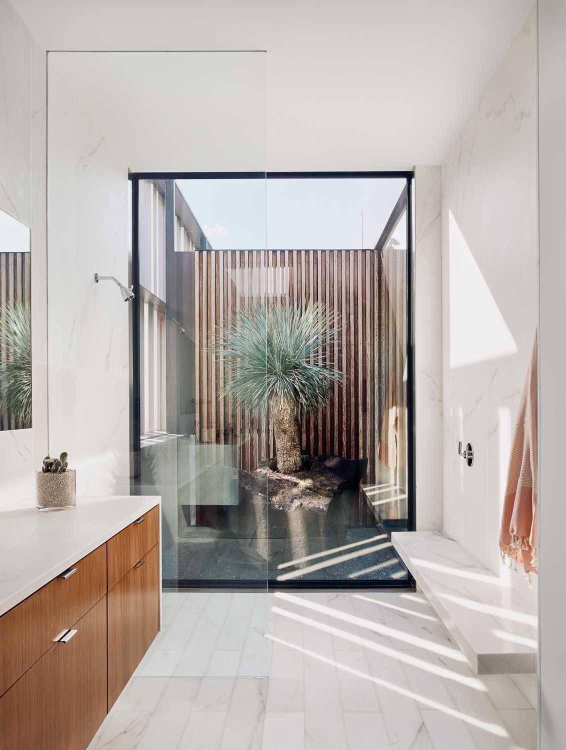 A floor-to-ceiling wood door opens to reveal the primary bedroom suite, which has two separate walk-in closets, as well as the bathroom split in two, one with a shower and freestanding bathtub, and the other with a shower that includes a large window.