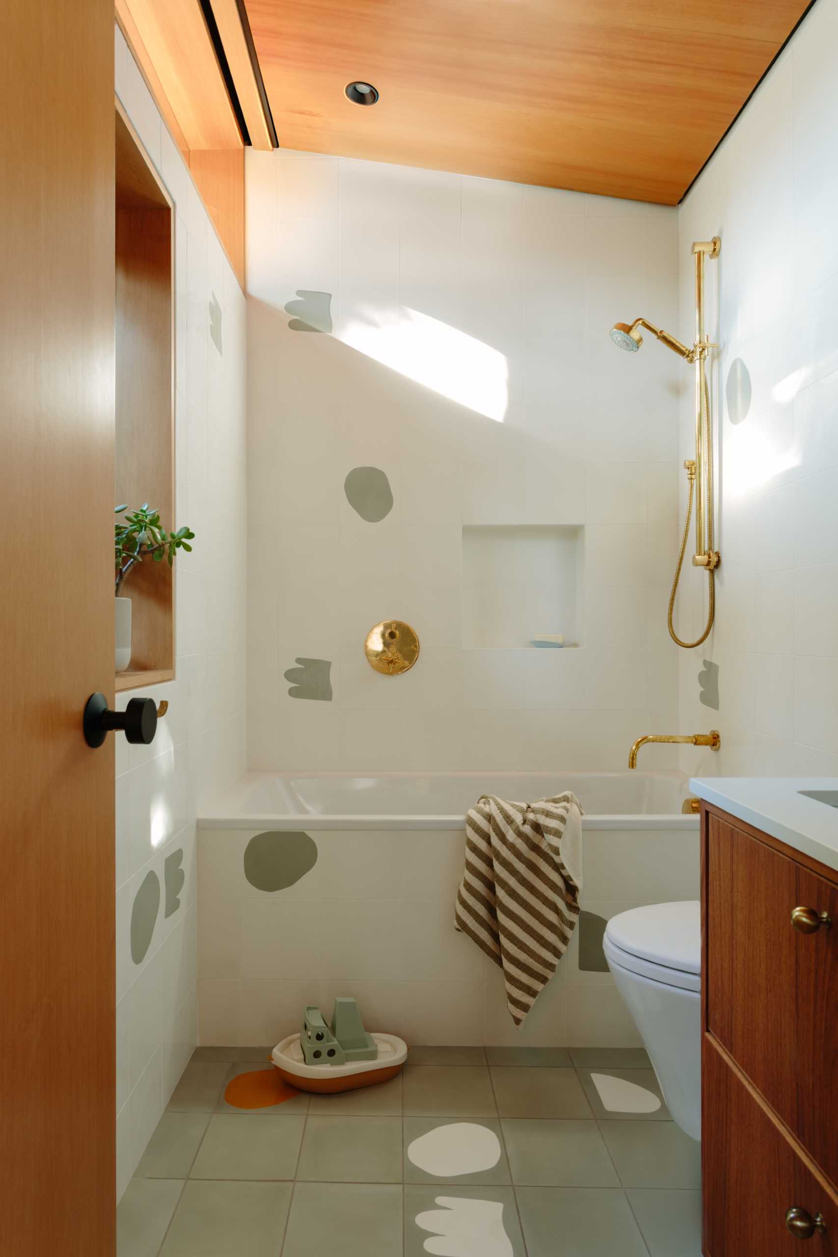 A bathroom in a renovated mid-century-modern home has a wood vanity, and fun graphic tiles.