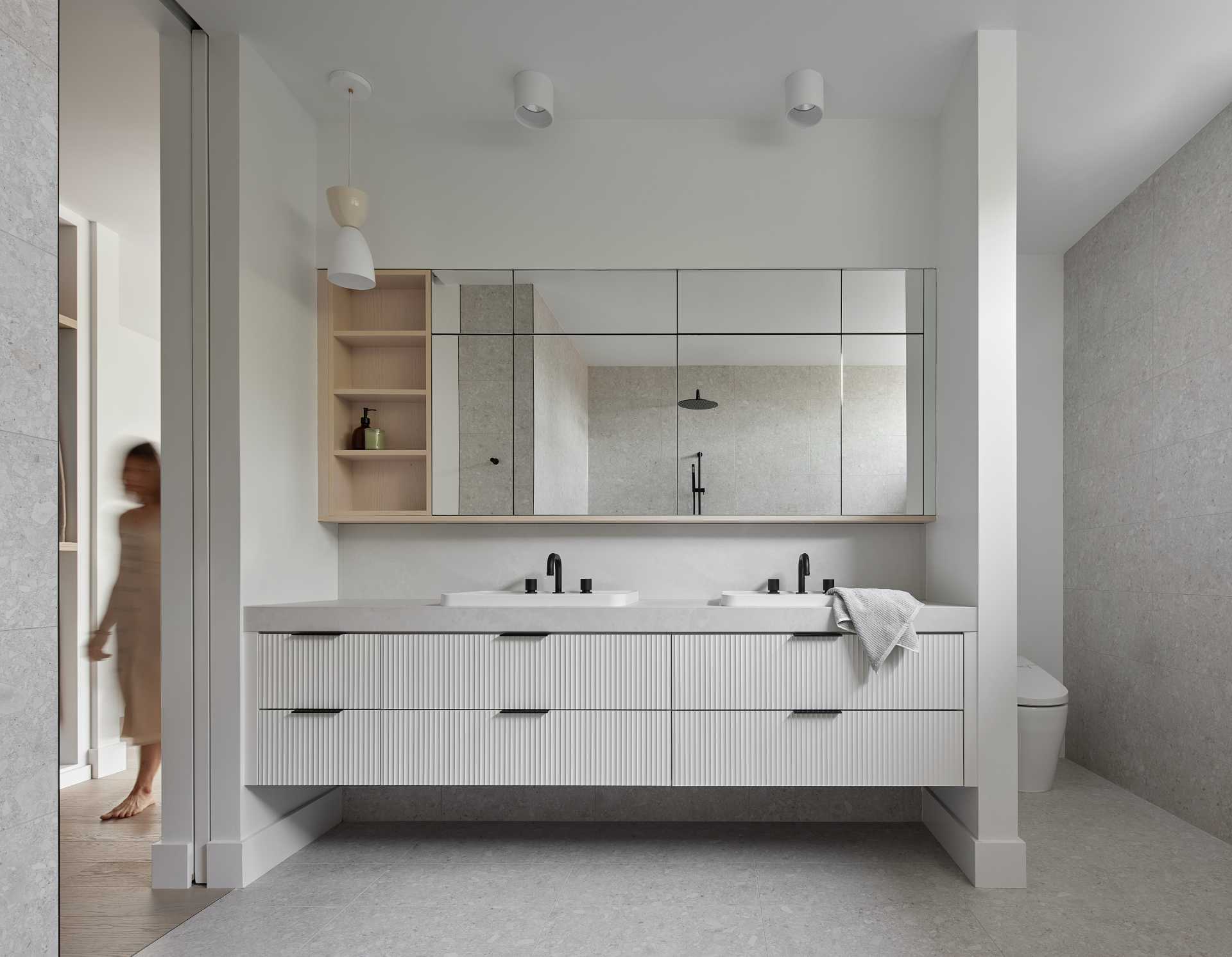 This modern primary en-suite bathroom has a double-vanity, a freestanding bathtub, and a shelving niche that runs the width of the wall.