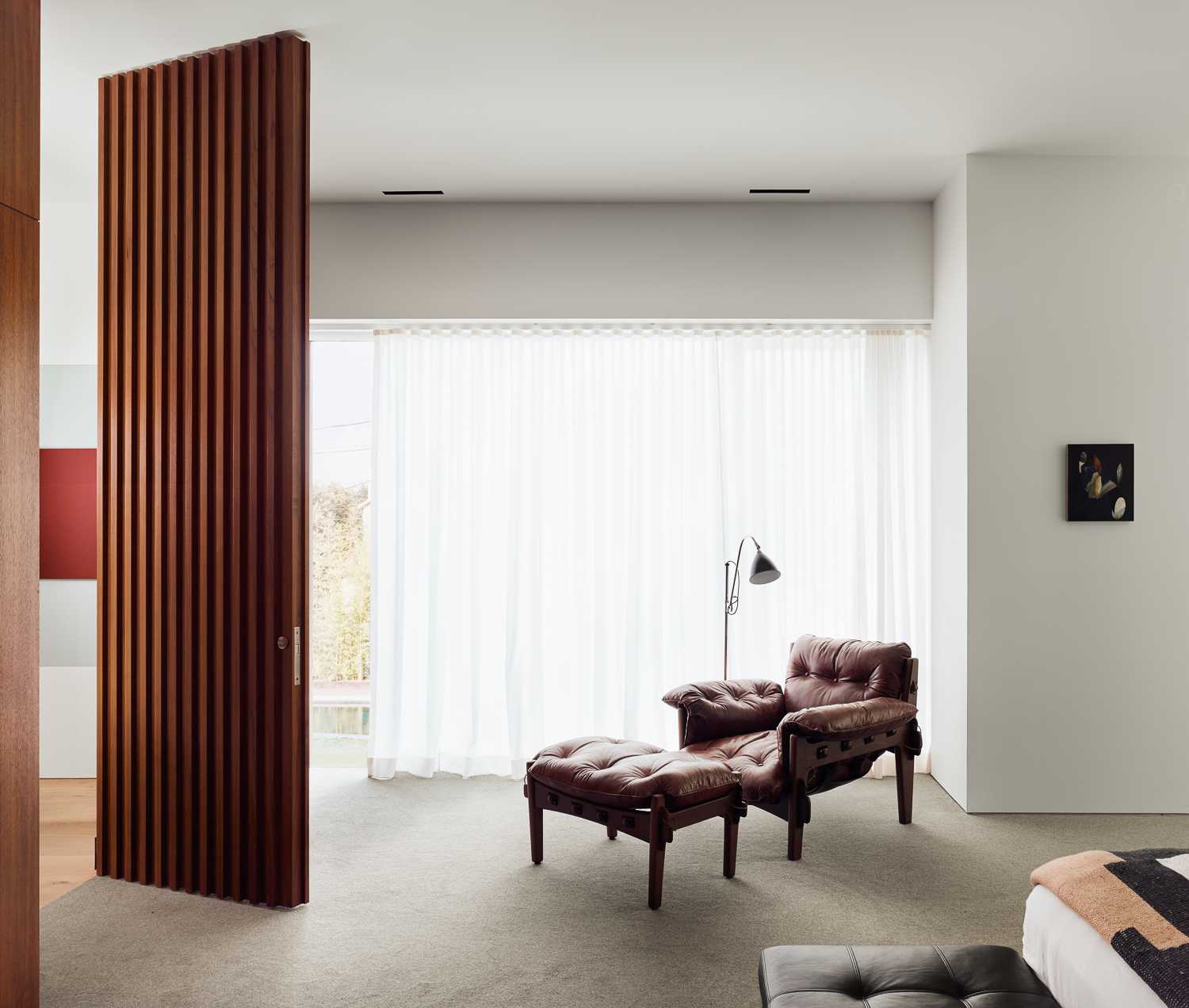 A floor-to-ceiling wood door opens to reveal the primary bedroom suite, which has two separate walk-in closets, as well as the bathroom split in two, one with a shower and freestanding bathtub, and the other with a shower that includes a large window.