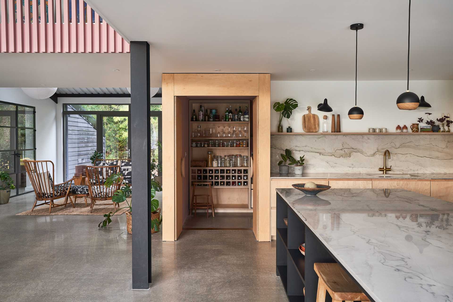 This modern black kitchen has a brass backsplash and an island with shelving for cookery book storage, while plywood has been used for the larder (pantry).